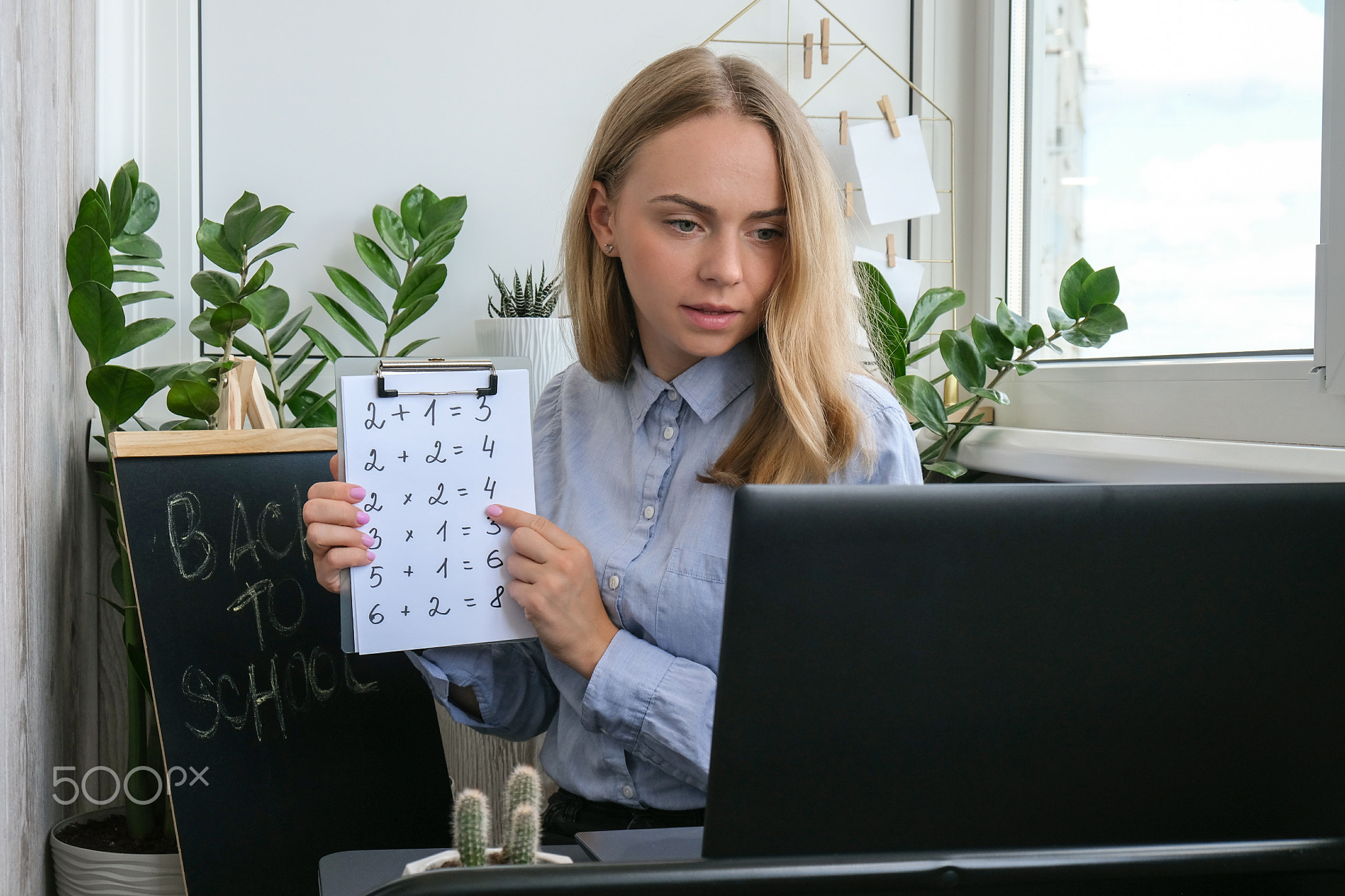 Young female teacher sitting at desk and using laptop teaching
