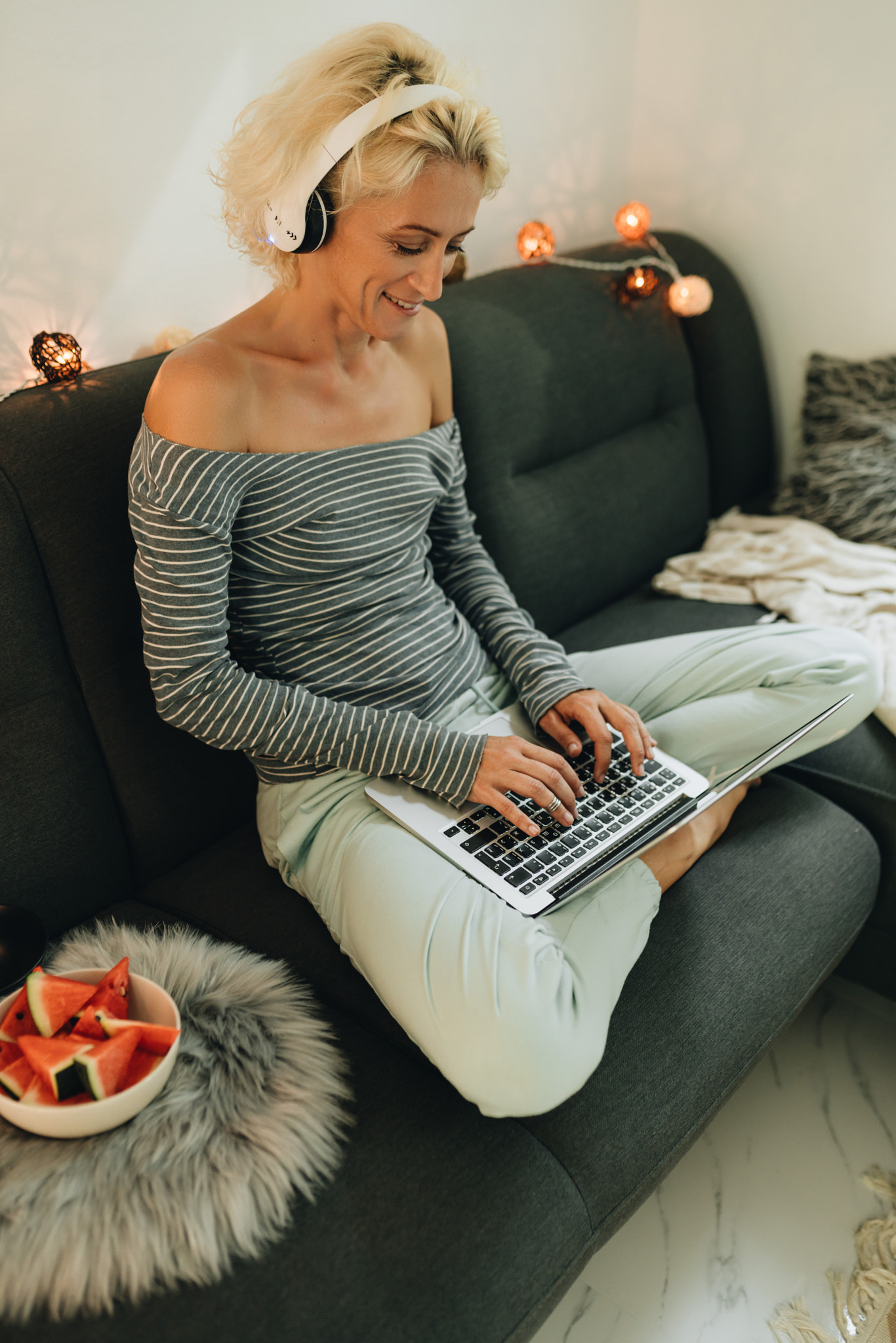 Adult woman in headphones sitting on a sofa and working by laptop