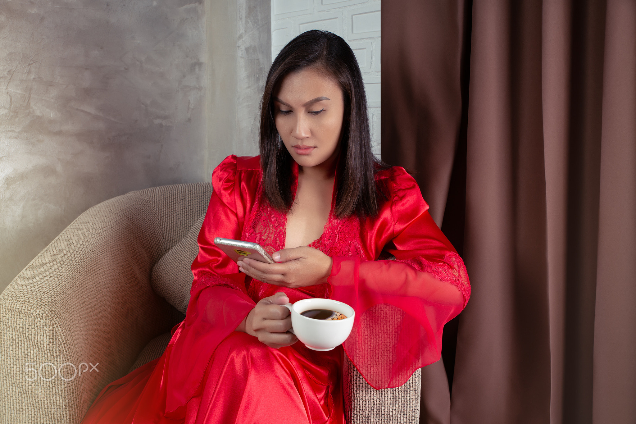 Woman in red satin nightgown looking at a smartphone.