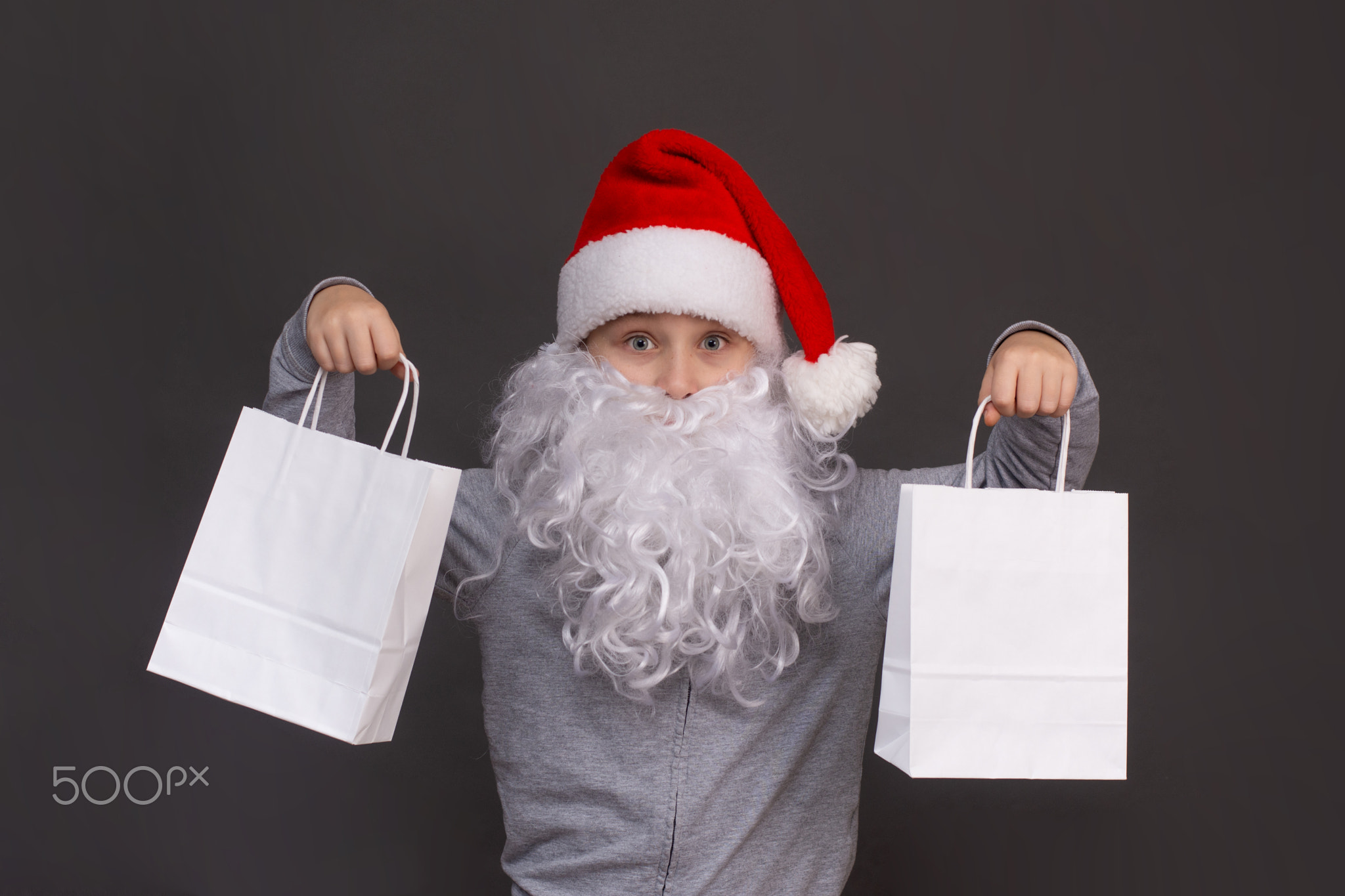 little Santa boy is holding two white paper bags in his hands. on a