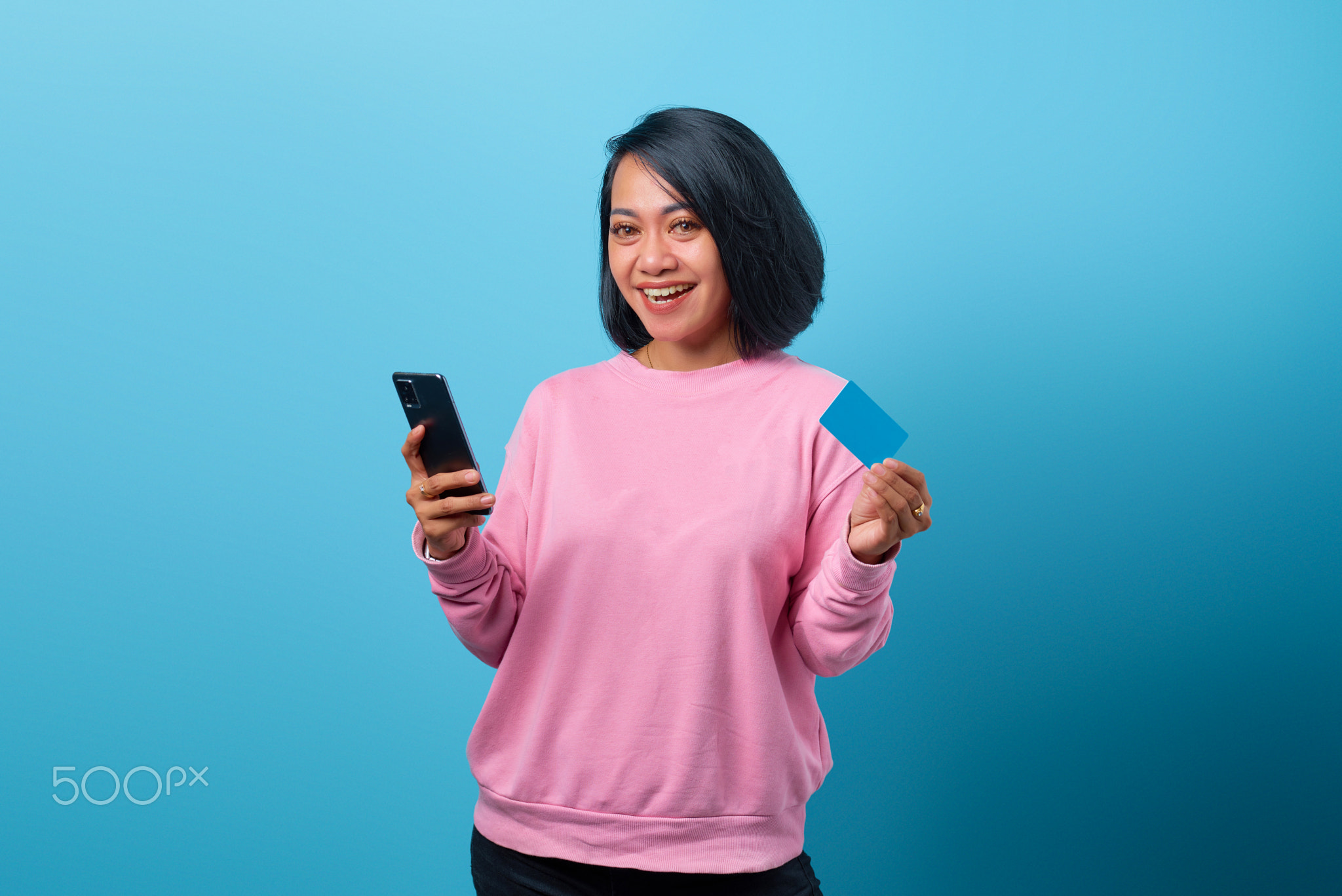 smiling asian woman using mobile phone and holding credit card