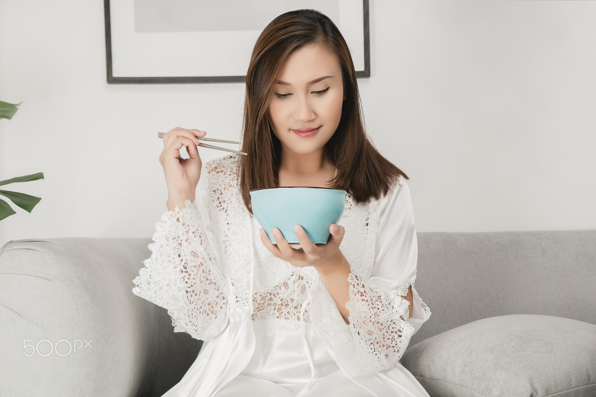 A woman wearing silk nightwear and lace robe eating Instant noodles