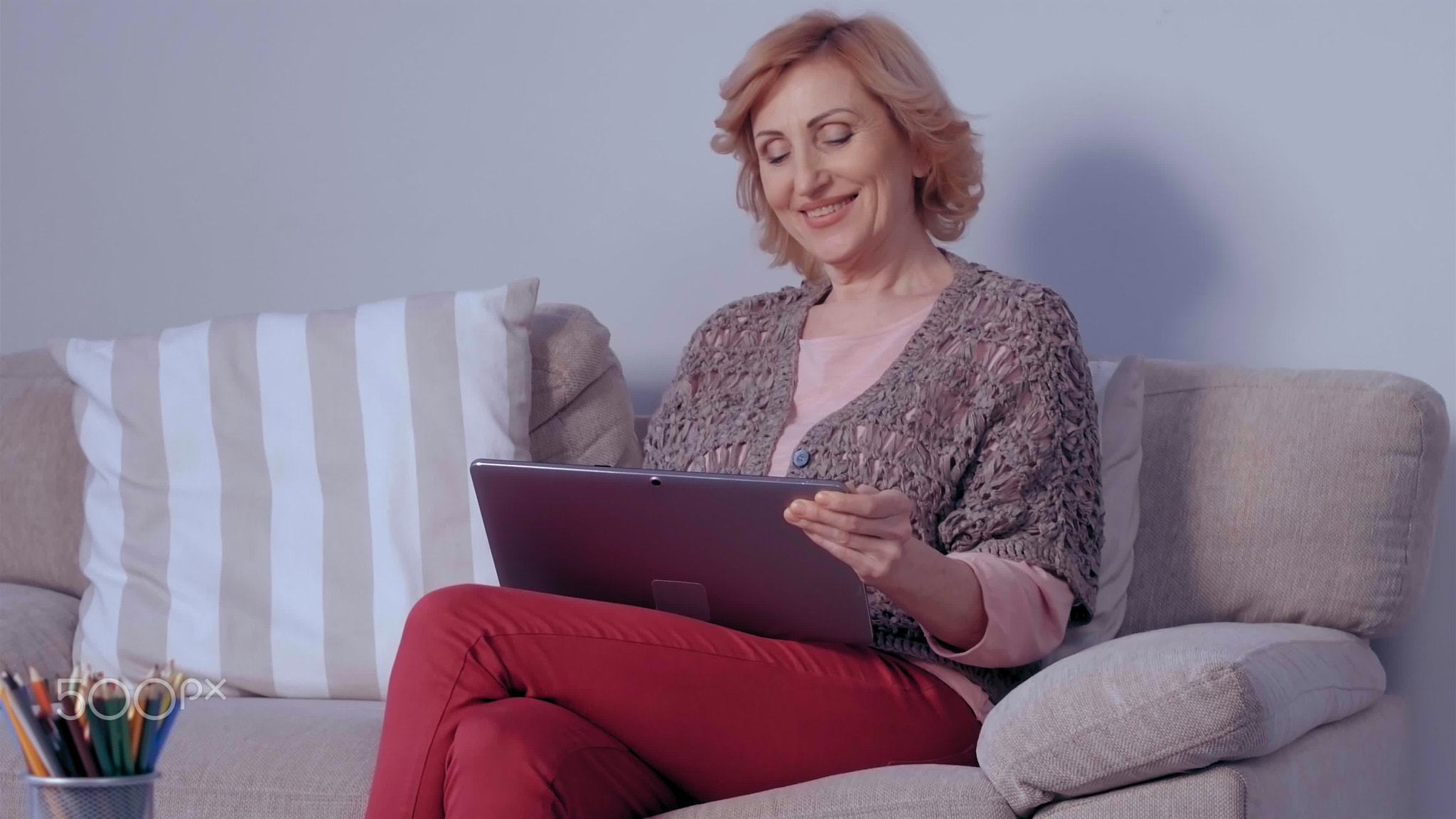 Happy mature woman sitting on her couch. She's got a laptop in her
