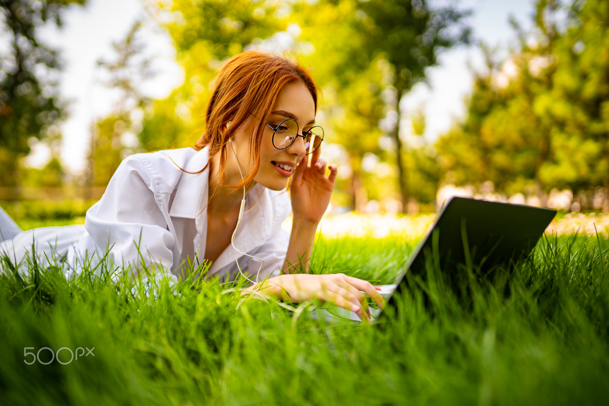 young redhead businesswoman lying on the grass in natural park uses