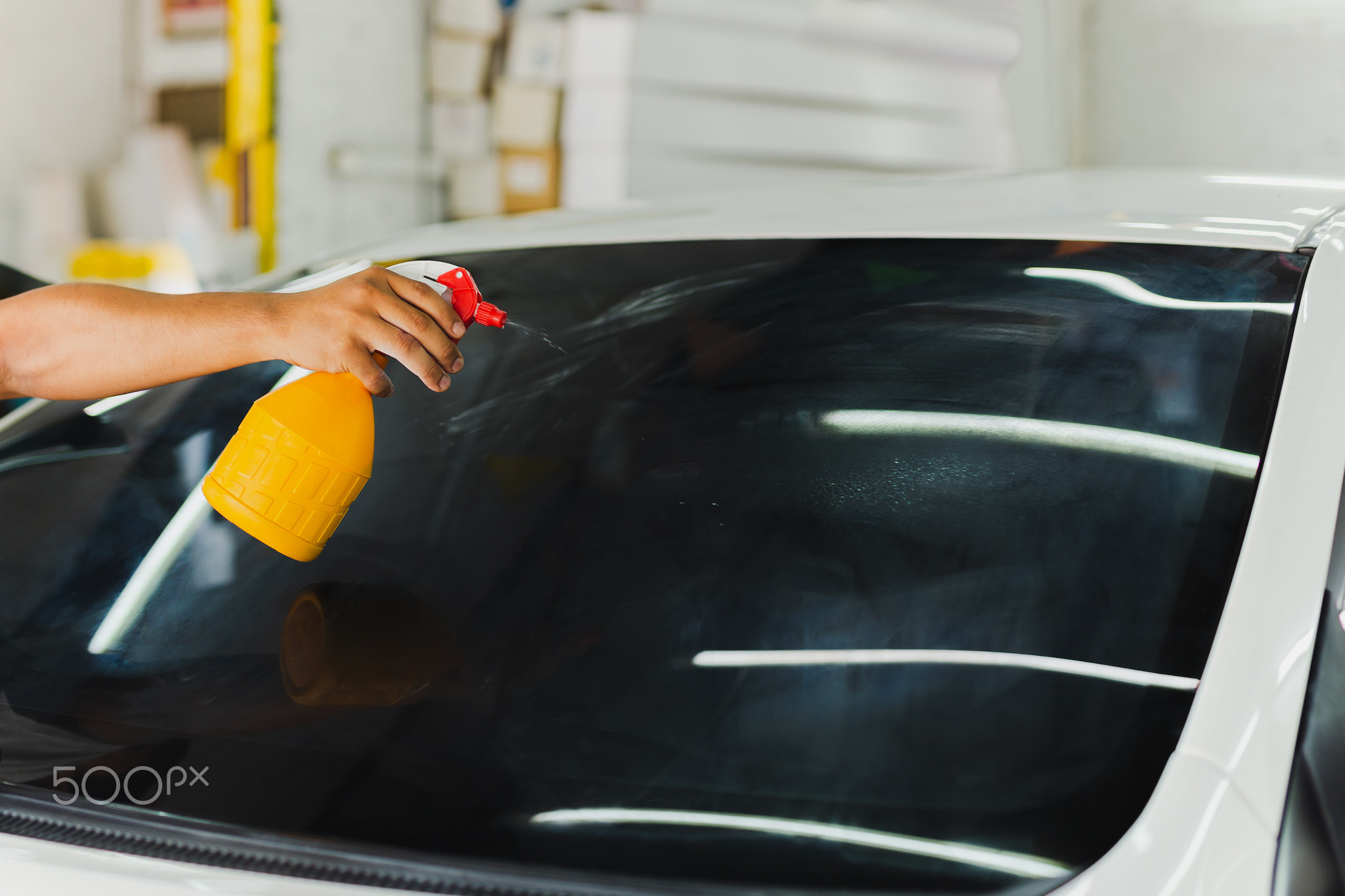 Car specialist spraying water into tinted car window in workshop.