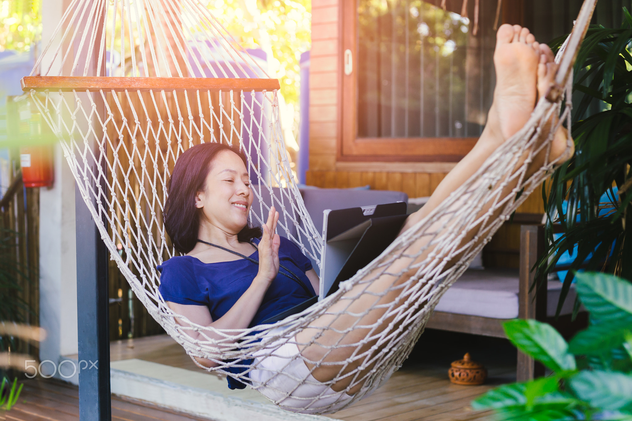 Happy successful woman lying in hammock waving and smiling while