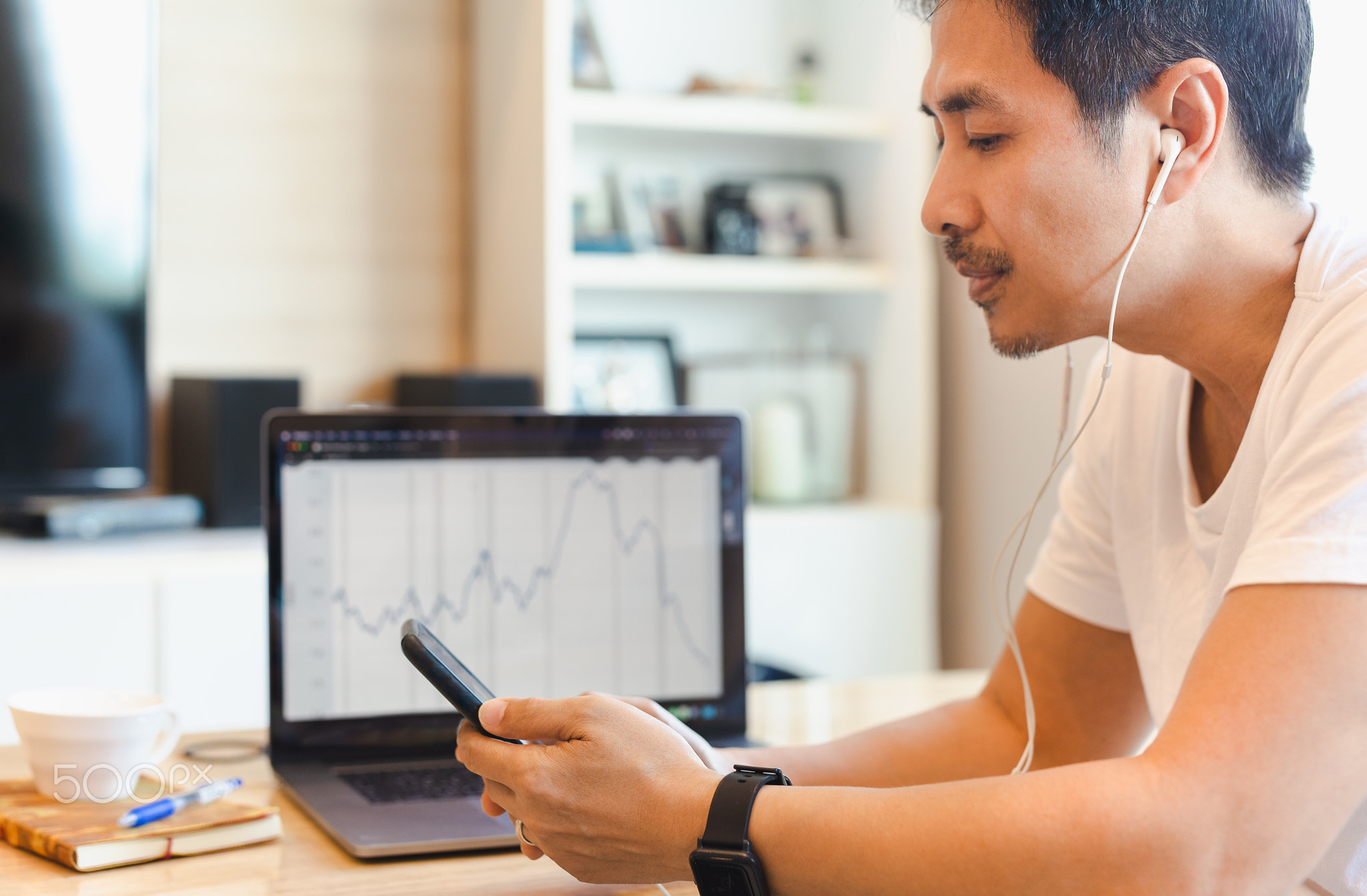 Businessman in glasses using mobile phone while working on laptop at