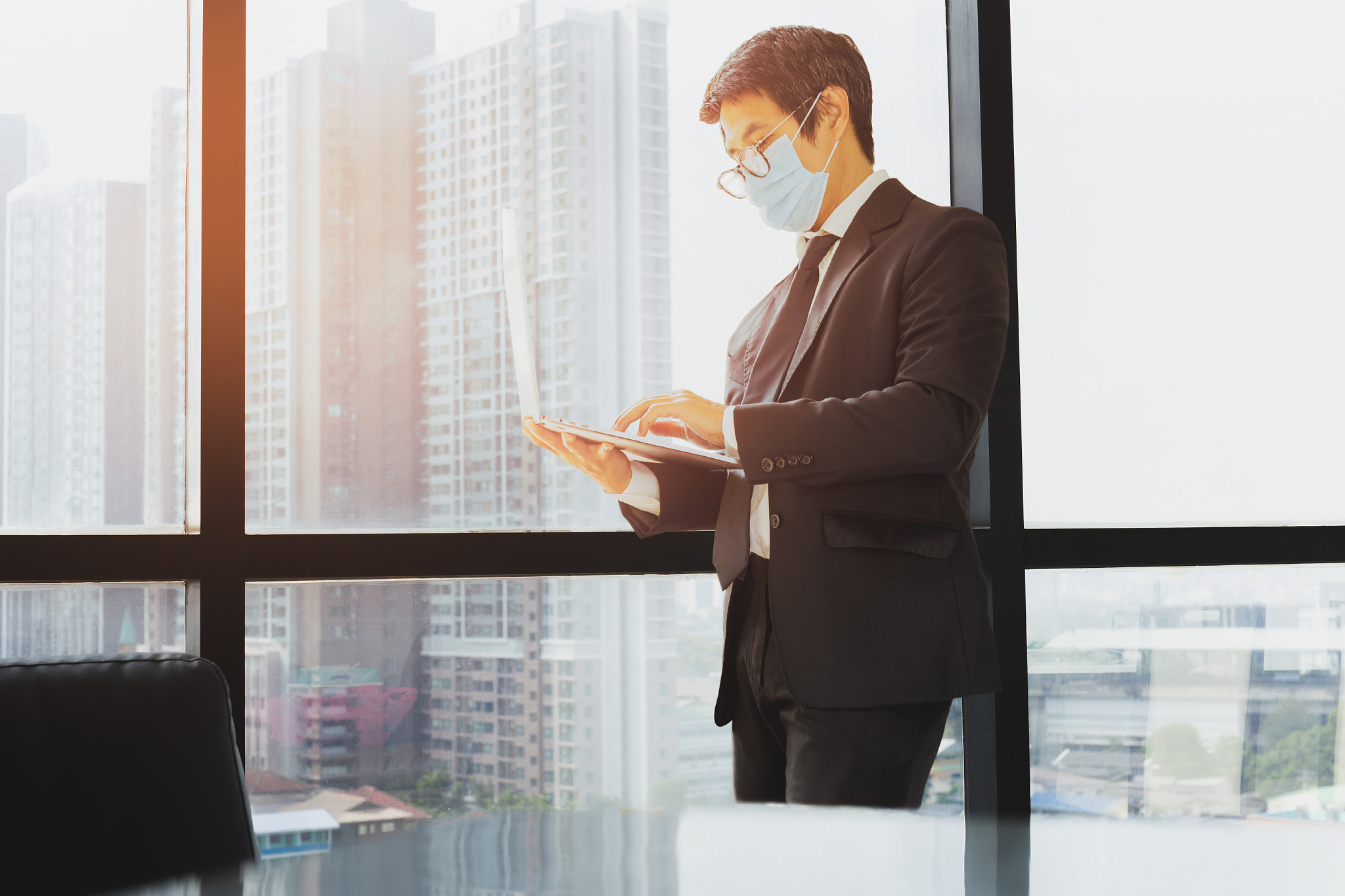 Asian businessman wears medical mask standing and holding laptop.