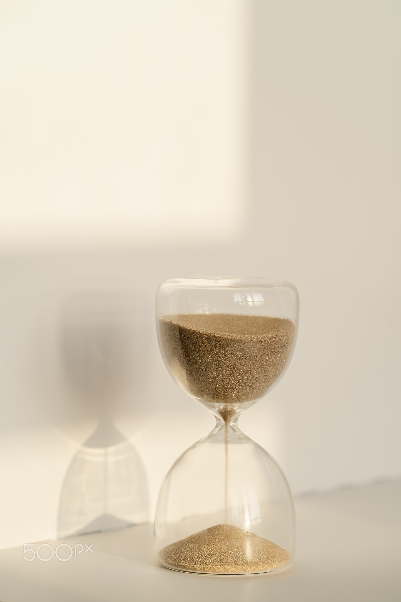 Transparent hourglass on a white sunny background.