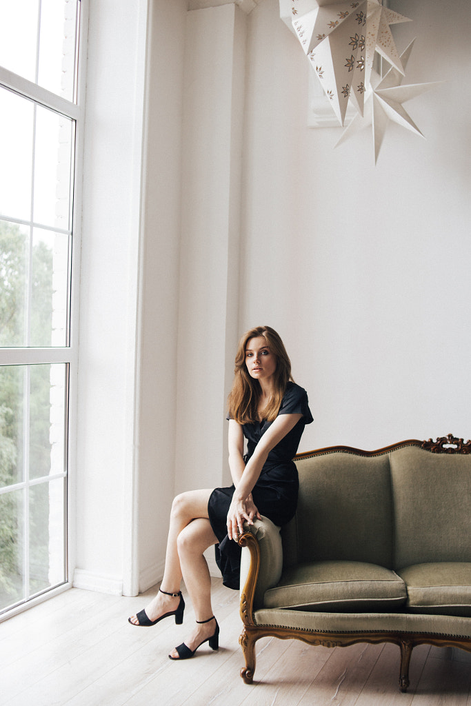 young girl in a black dress sits on a sofa in front of a window by Alena Sadreeva on 500px.com