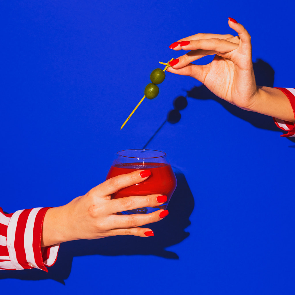 Female hand holding glass with cocktail isolated on bright blue neon by Volodymyr Melnyk on 500px.com