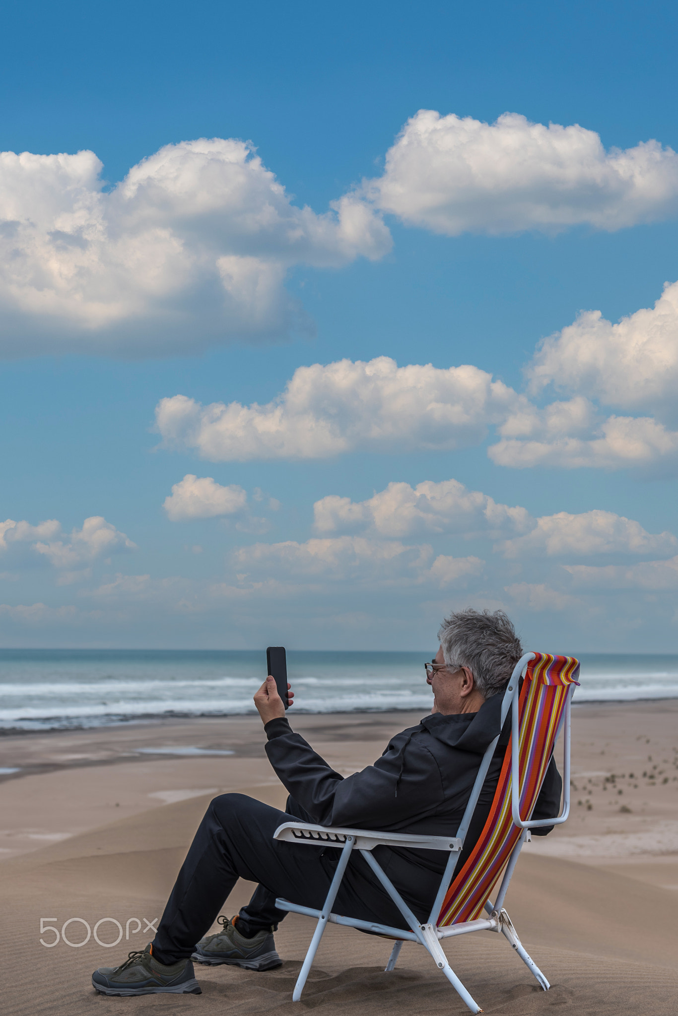 Mature adult male sitting on a beach chair on top of a dune facing the