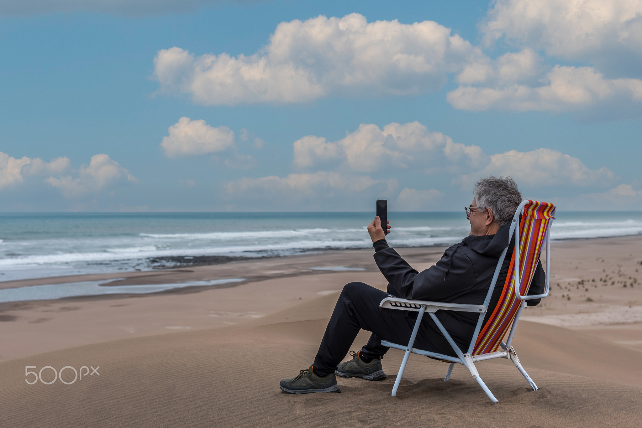 Mature adult male sitting on a beach chair on top of a dune facing the