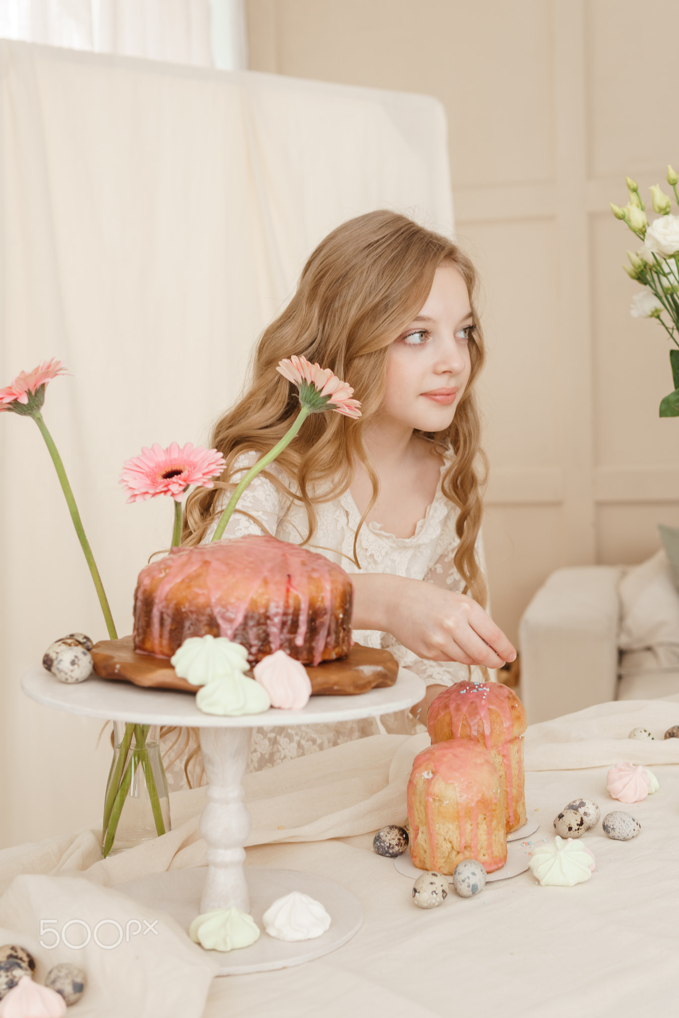 A girl with long hair in a light dress is sitting at the Easter table