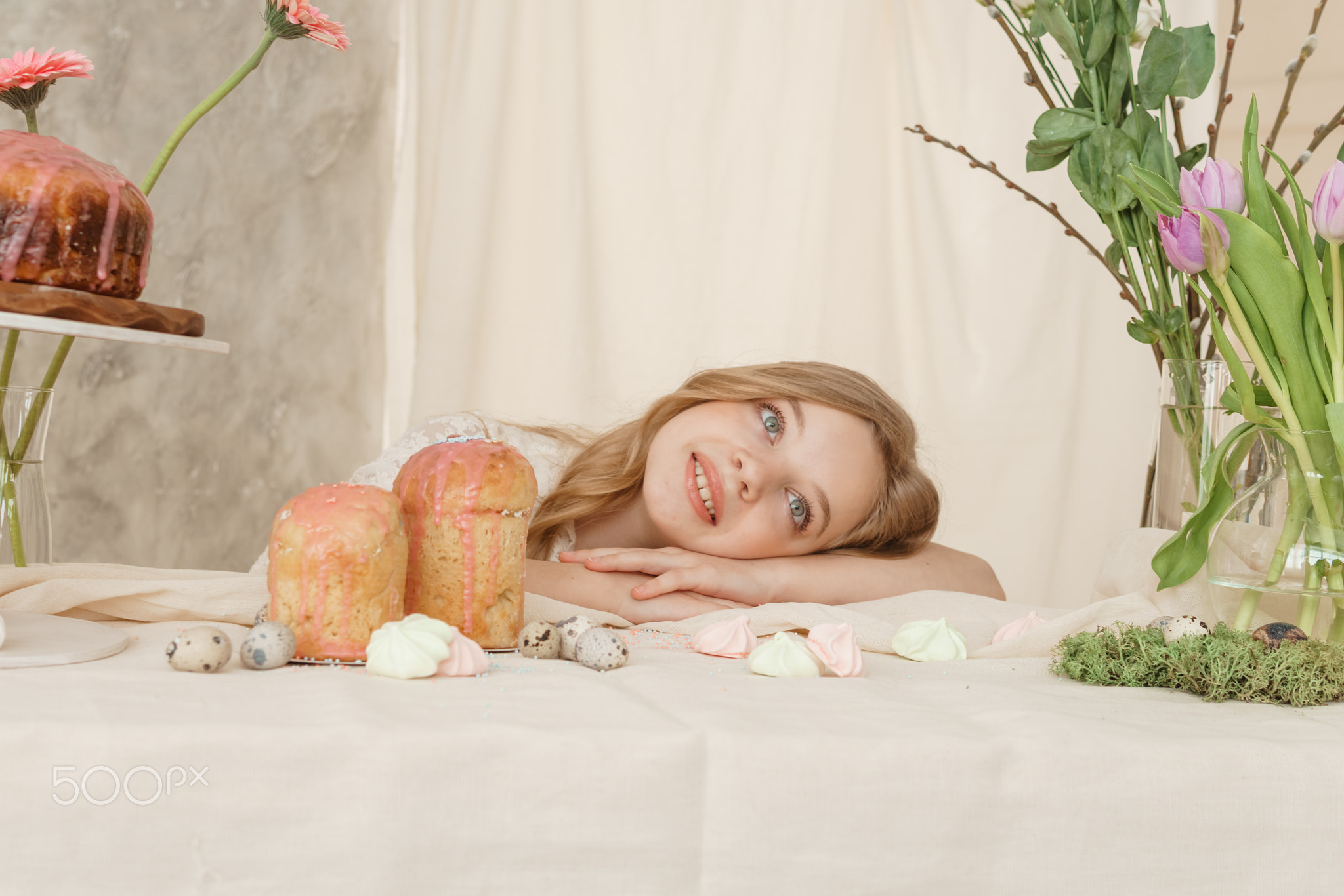 A girl with long hair in a light dress is sitting at the Easter table