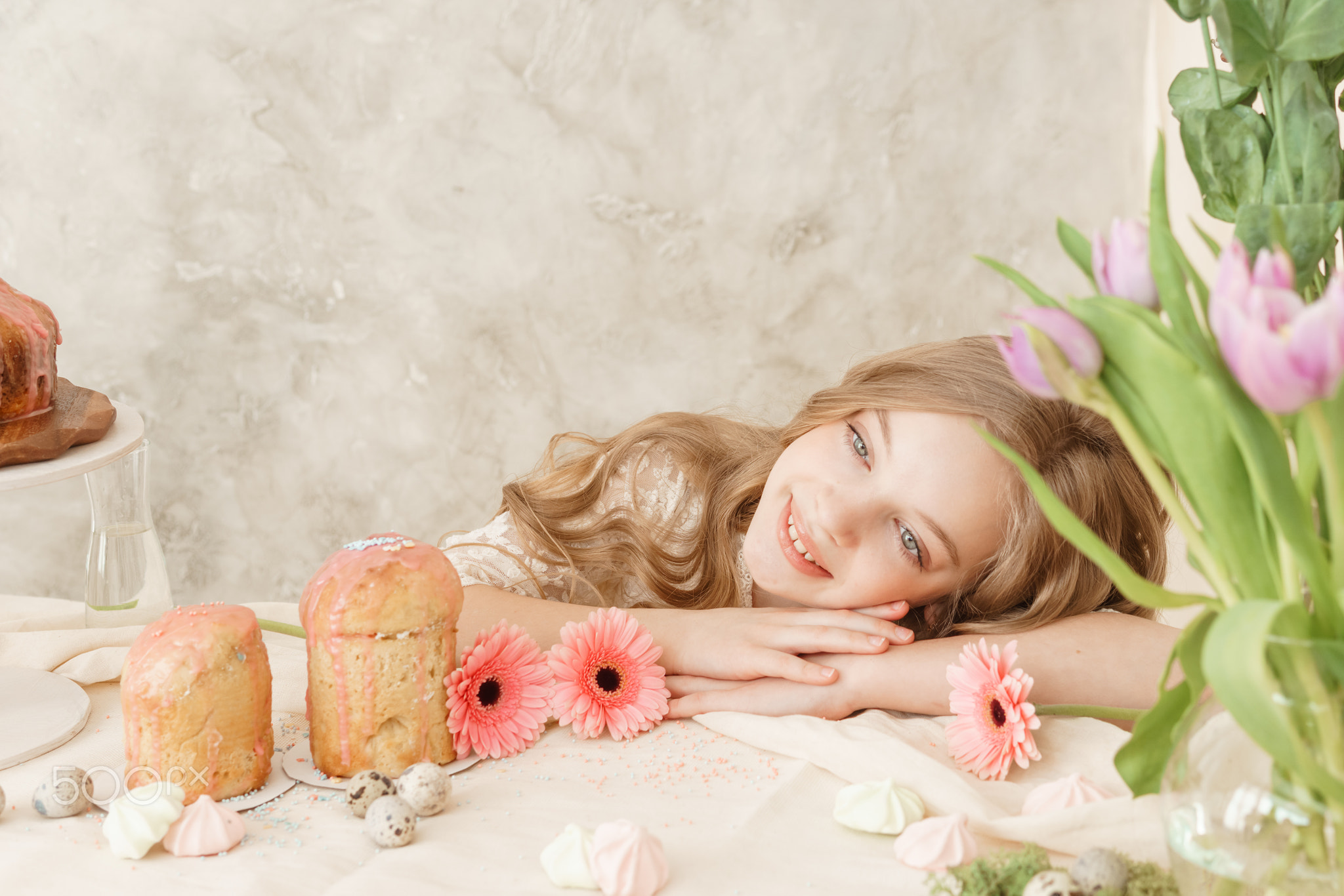 A girl with long hair in a light dress is sitting at the Easter table