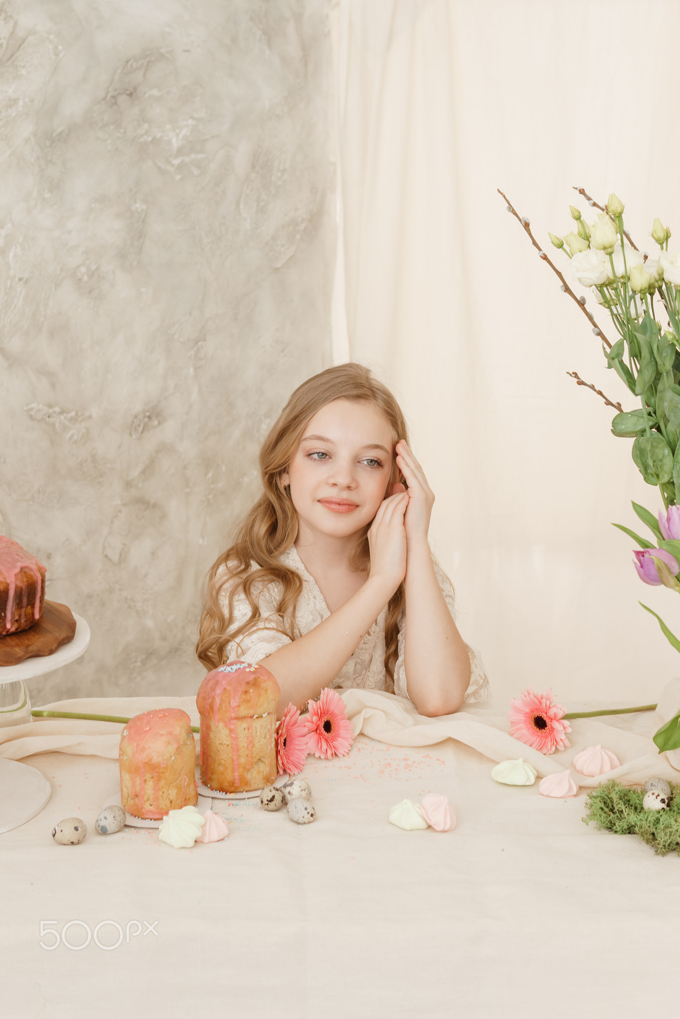 A girl with long hair in a light dress is sitting at the Easter table
