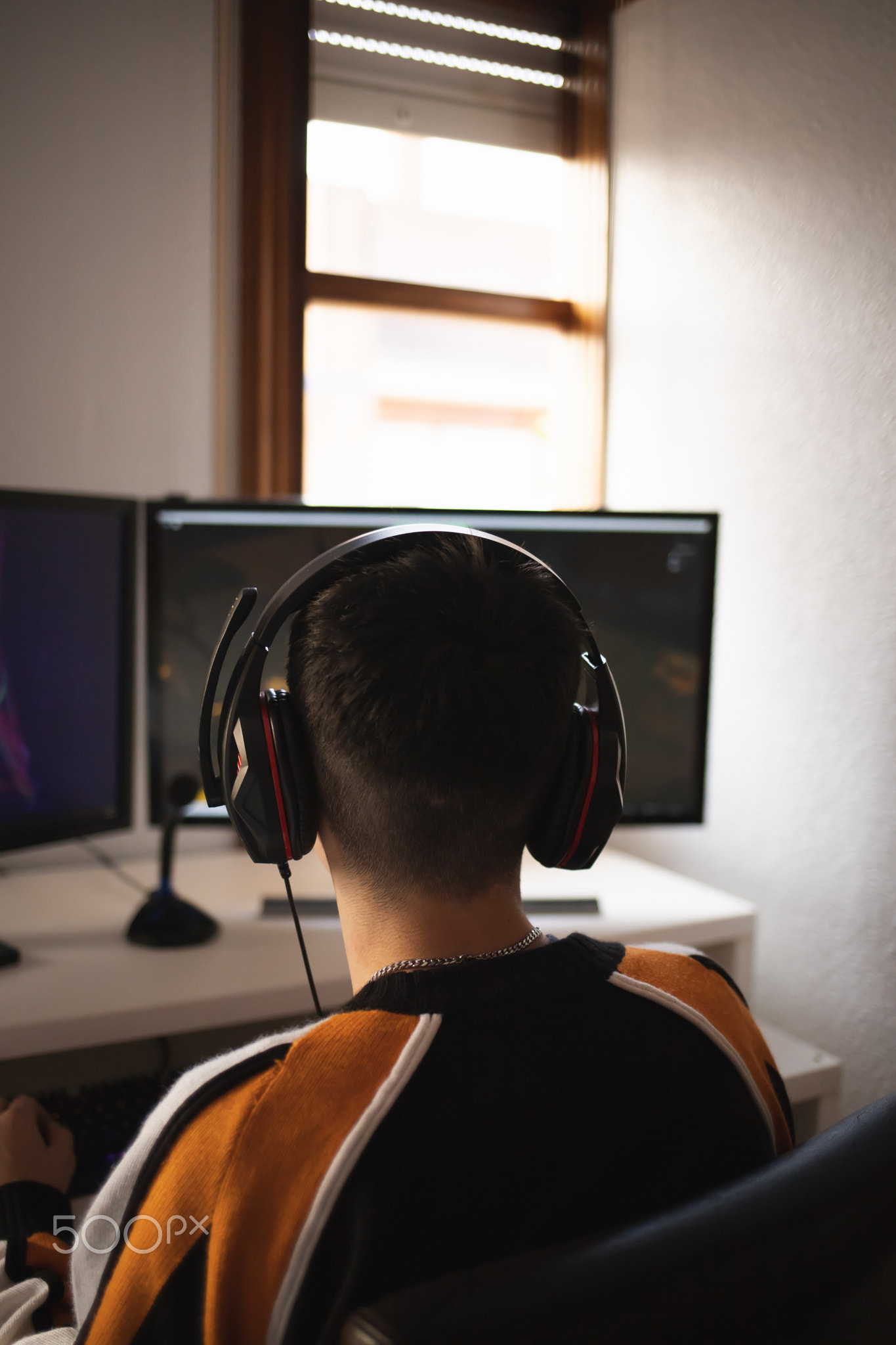 Back view of concentrated young gamer in headphones and glasses using