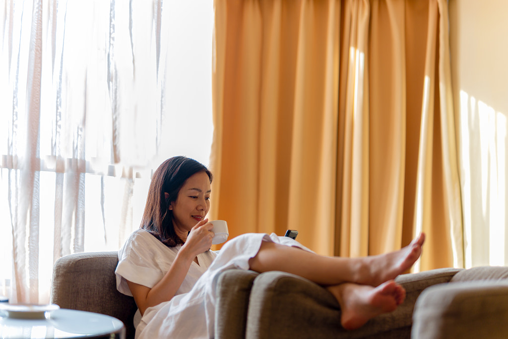 Woman sitting on couch looking at cell phone with coffee in her hand. by Suwinai Sukanant on 500px.com