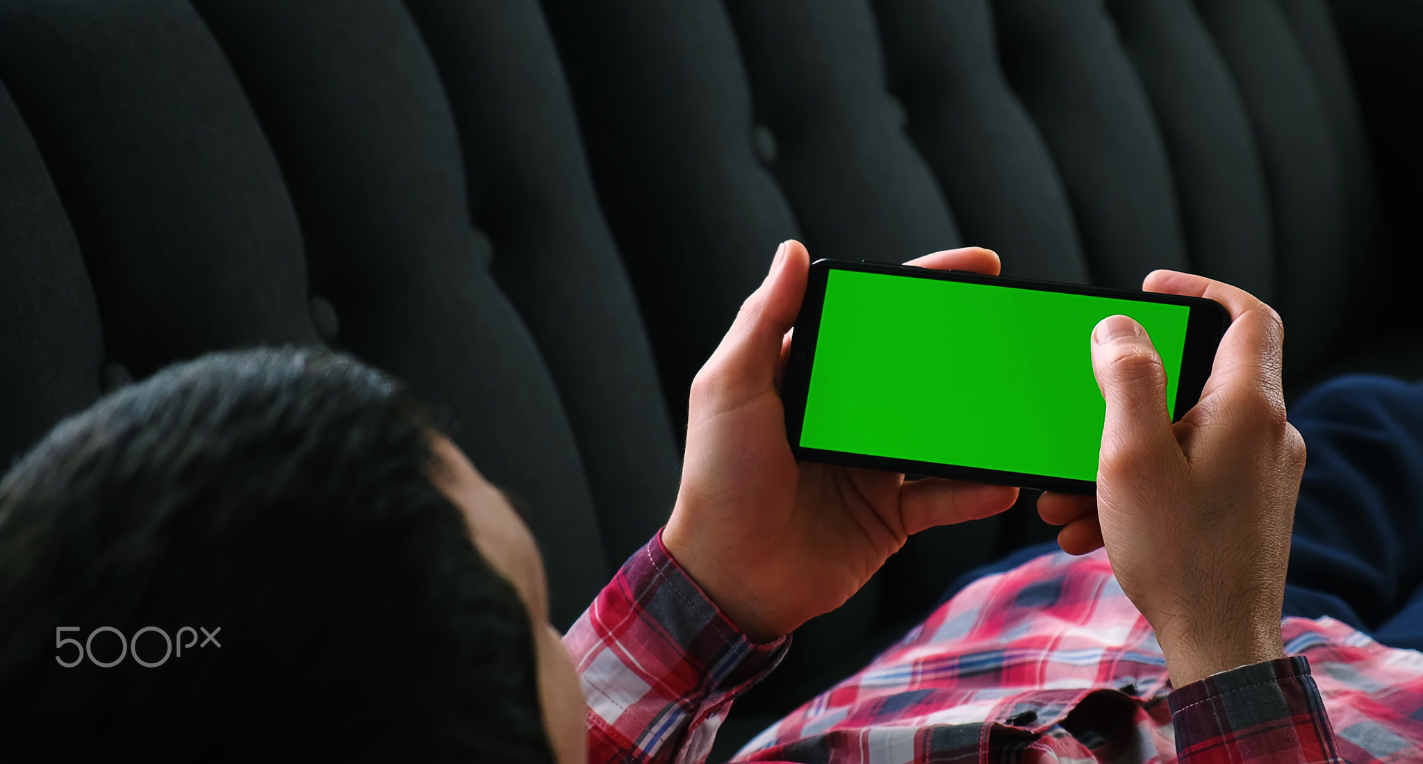 A man holds a phone in his hands with a green screen. Selective focus.