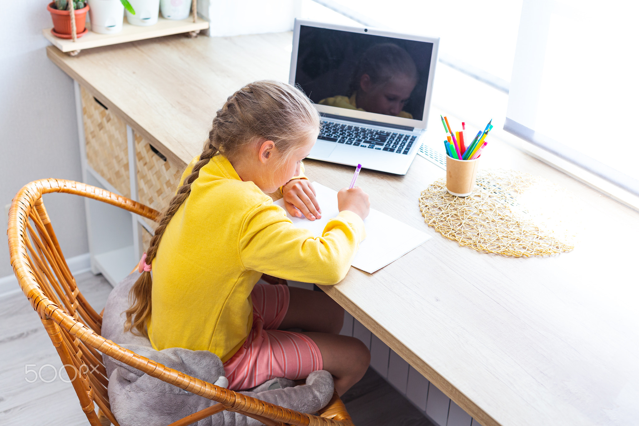 School girl in yellow sweatshirt is doing homework at home in front of