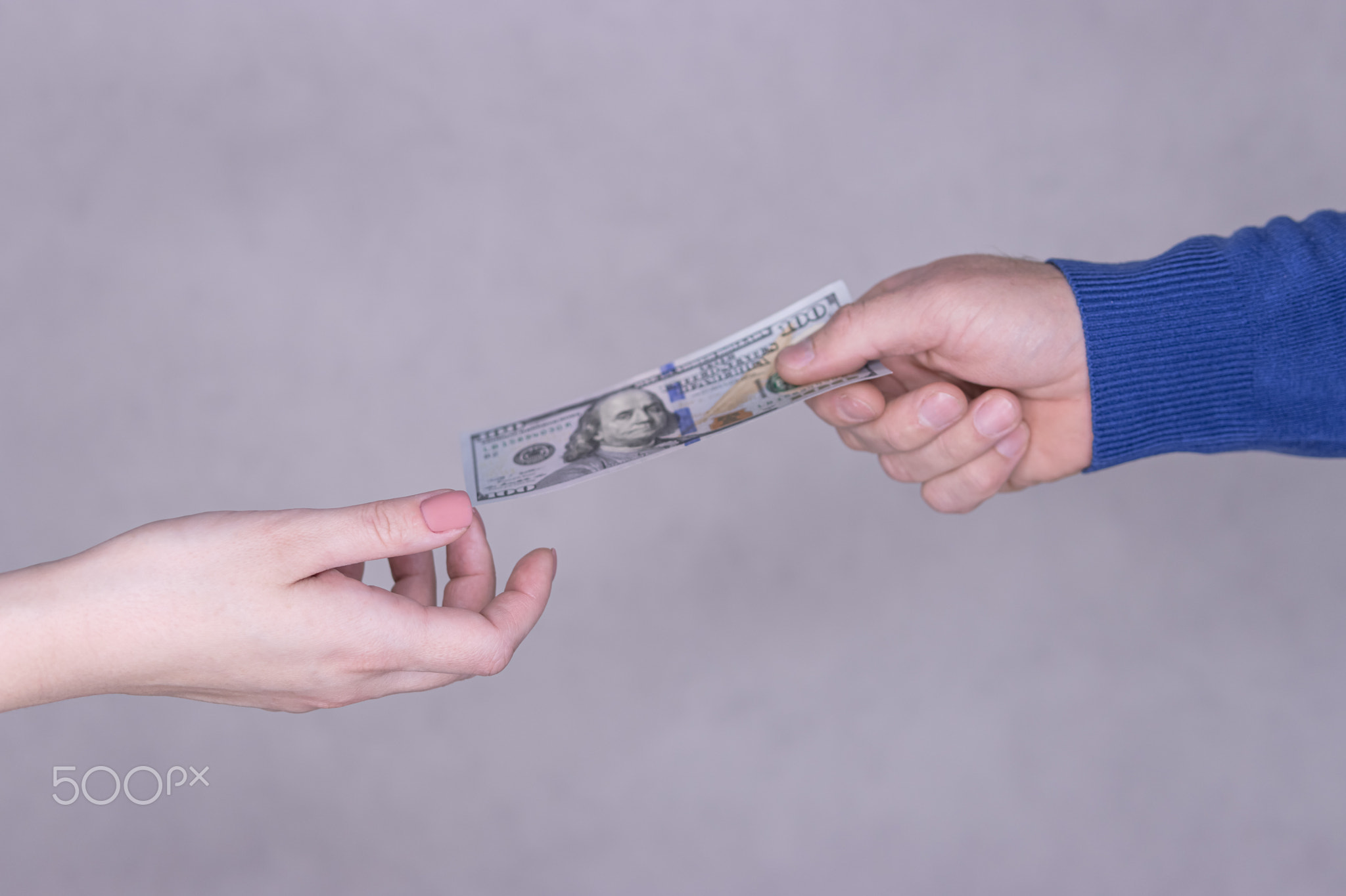 male hand gives 100 dollars to female hands on a gray background