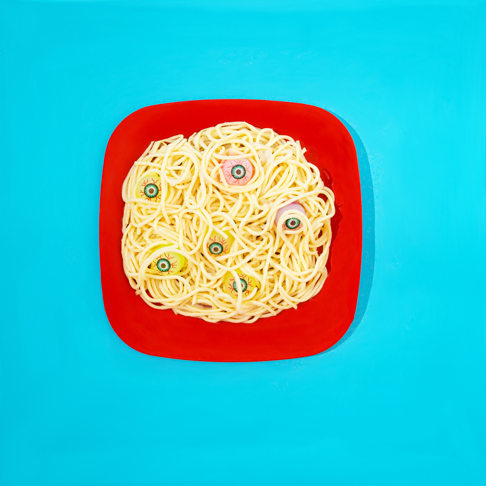 A red plate with spagetti and scary eye balls emerging from the food.