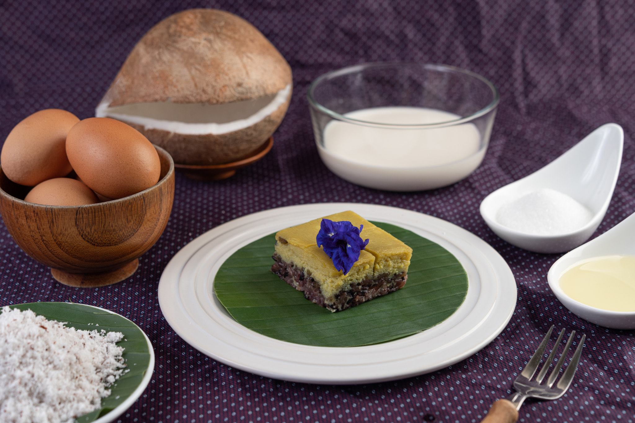 Black sticky rice and custard on a banana leaf in a white plate.: Black sticky rice and custard on a banana leaf in a white plate with butterfly pea flowers.