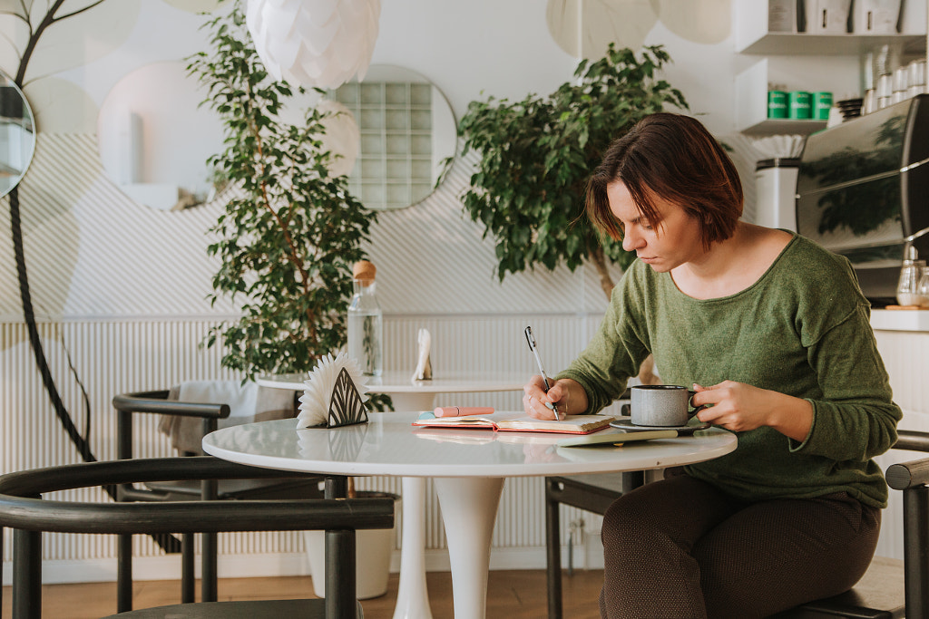 a young woman is sitting at a table in a cafe by Darya Vershinina on 500px.com