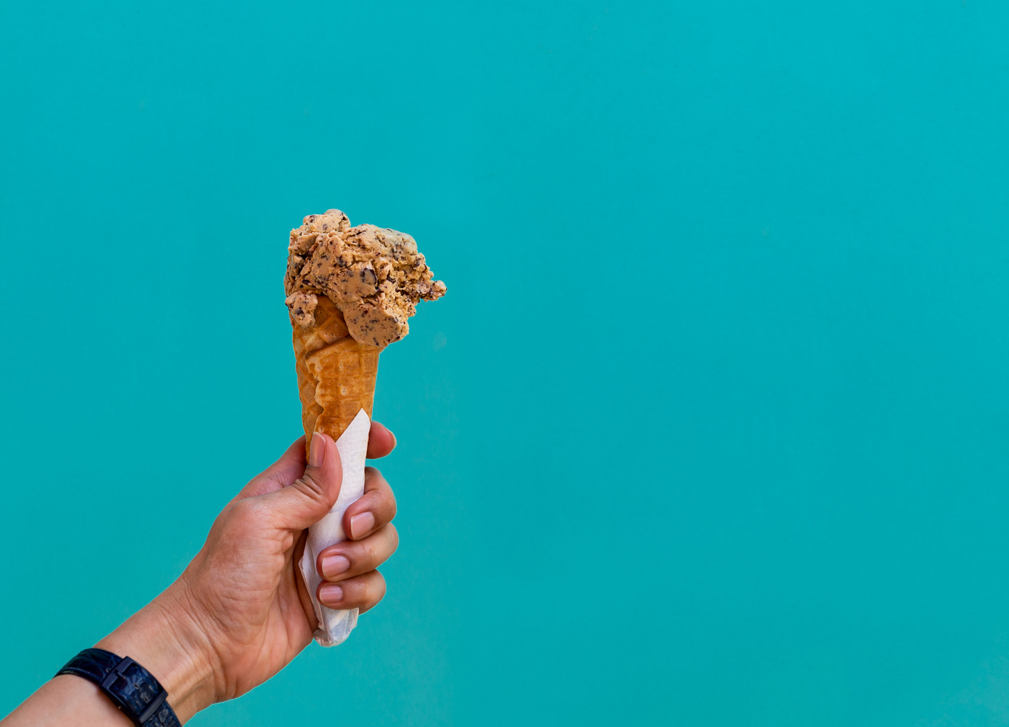 Female hand holding ice cream cone isolated on blue pastel background.