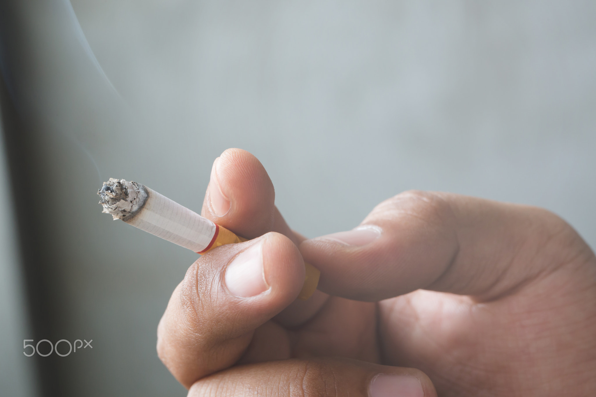 man holding smoking a cigarette in hand dark background.