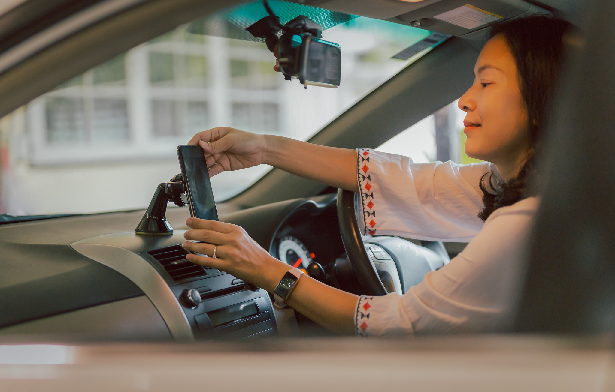 Woman driver hand adjust cell phone in stand holder for direction.