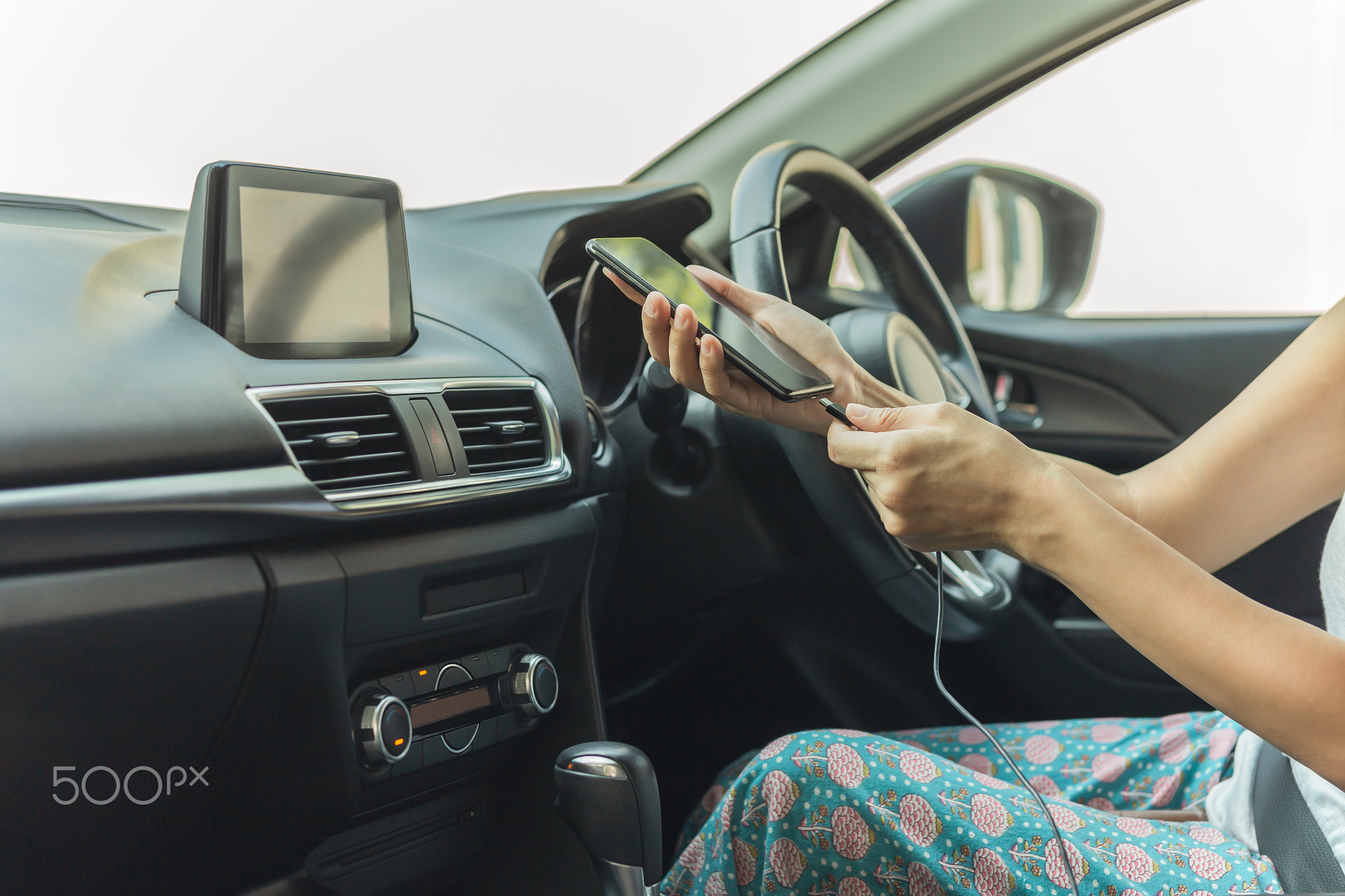 Woman driver charging her smart phone in the car.