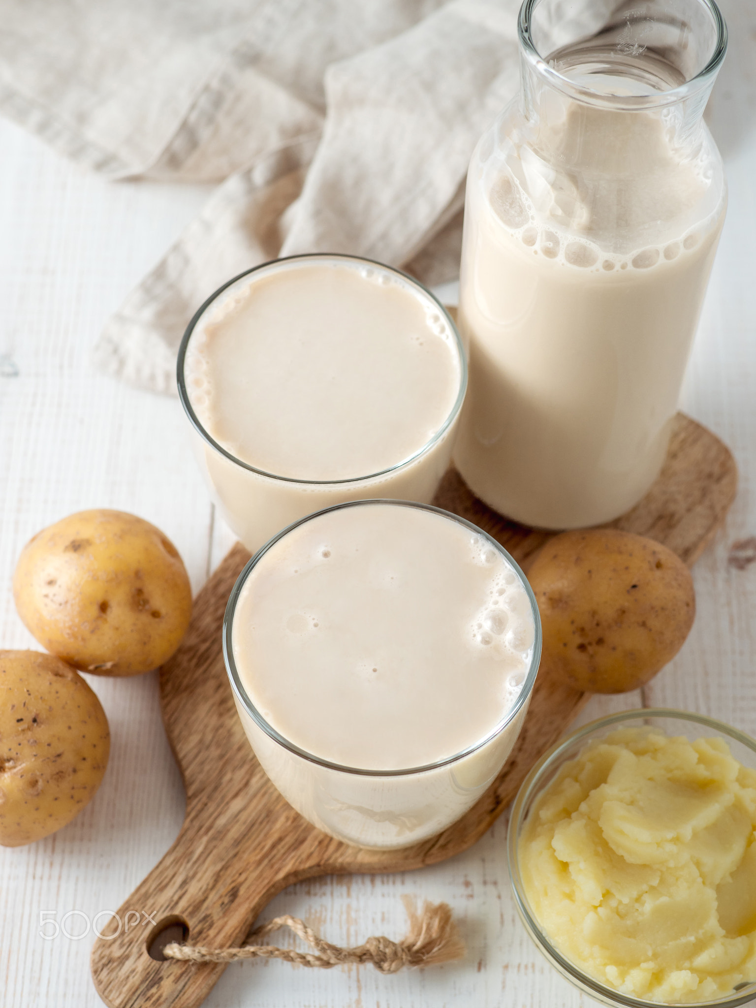 Potato milk pouring into glass on white wooden bg