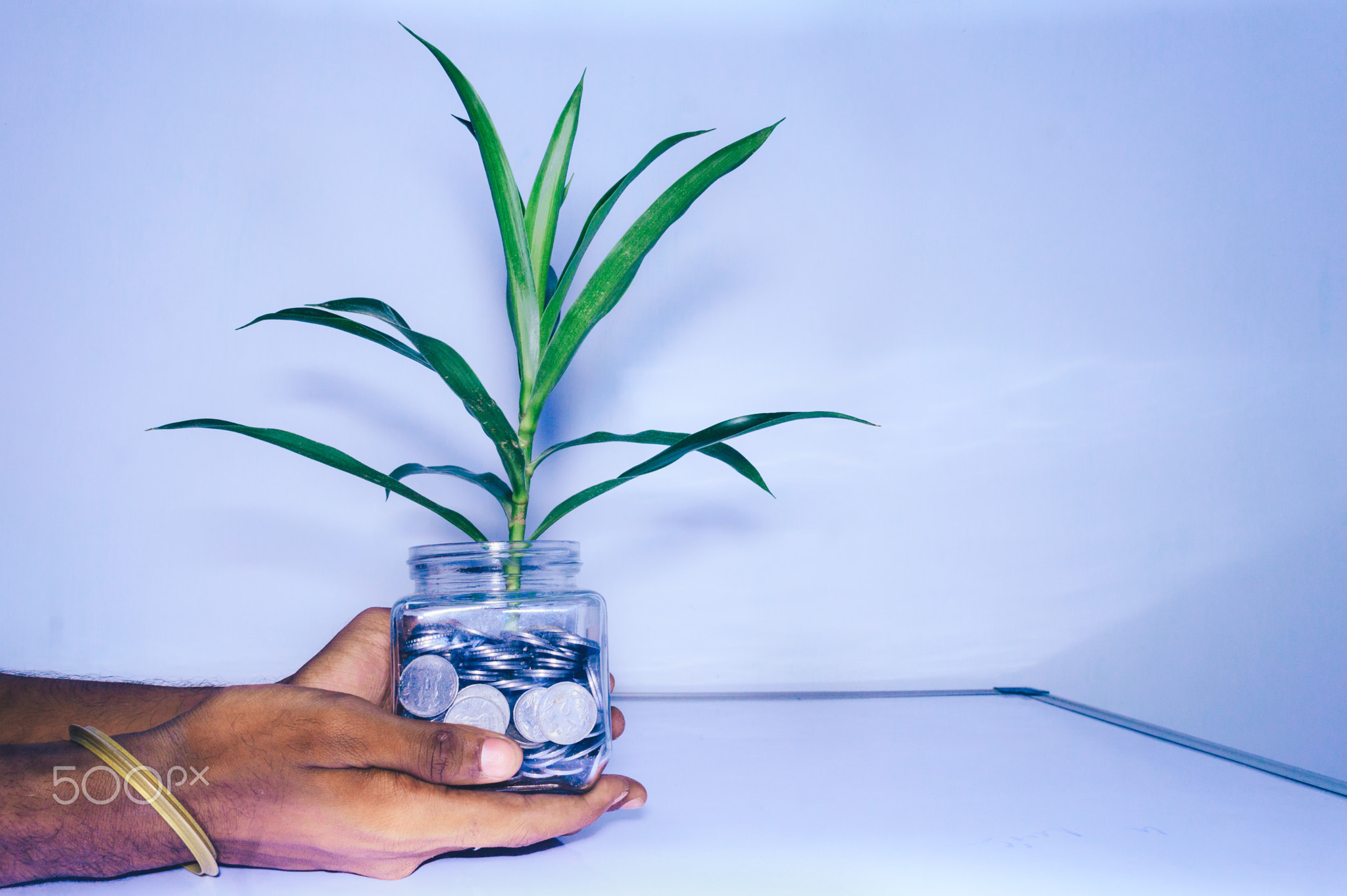 Human hand holding a glass jar full of coins on white background.