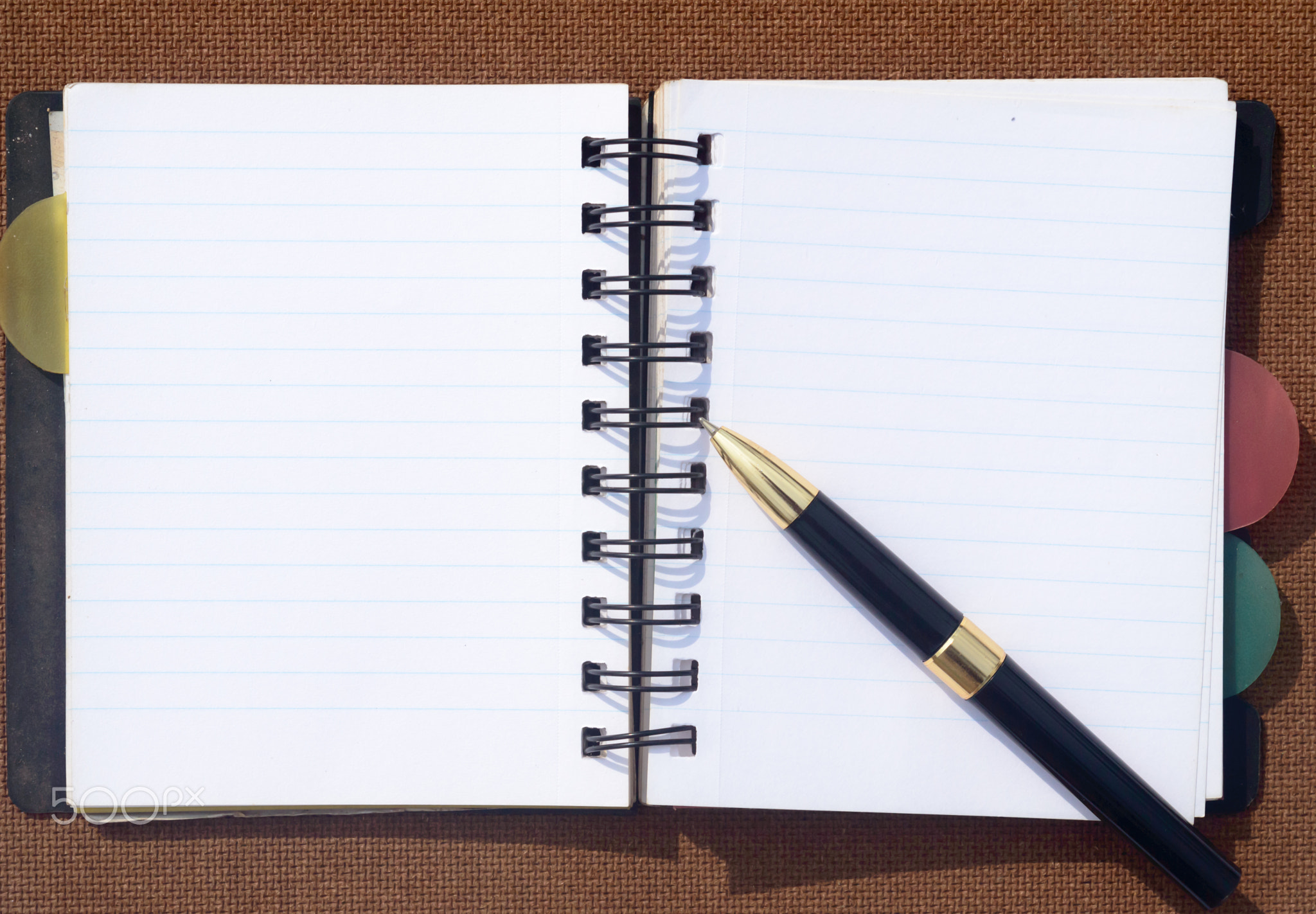 A pen placed over open notebook on Brown Color Hard cork board