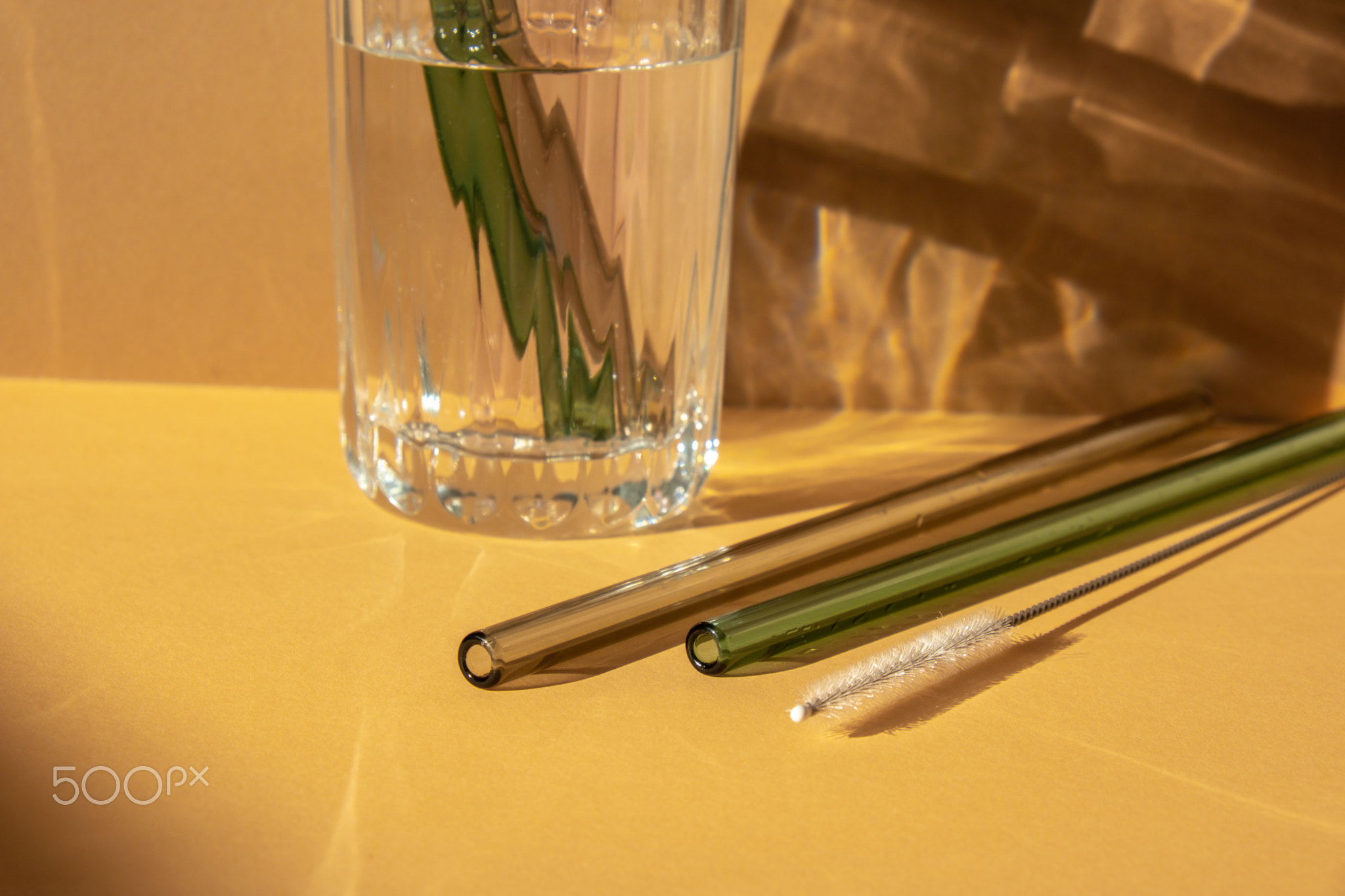 Reusable glass Straws in Glass with water on beige neutral background