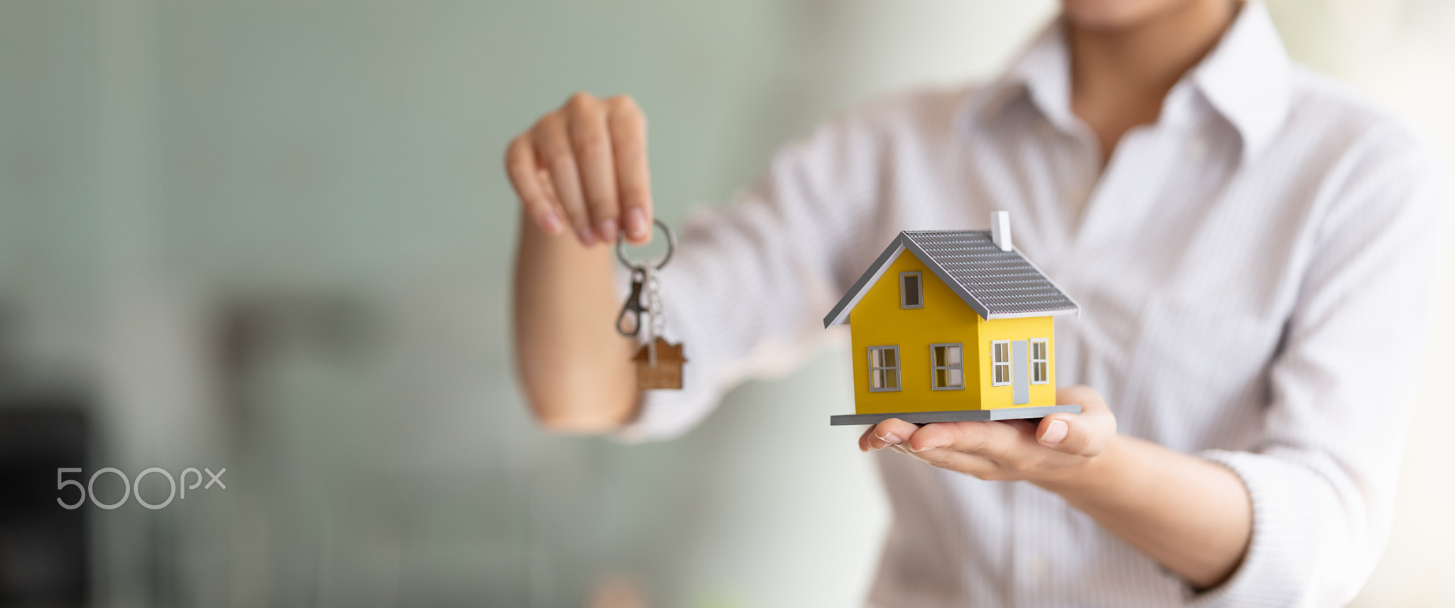 Cropped shot of real estate agent handing keys and home model.