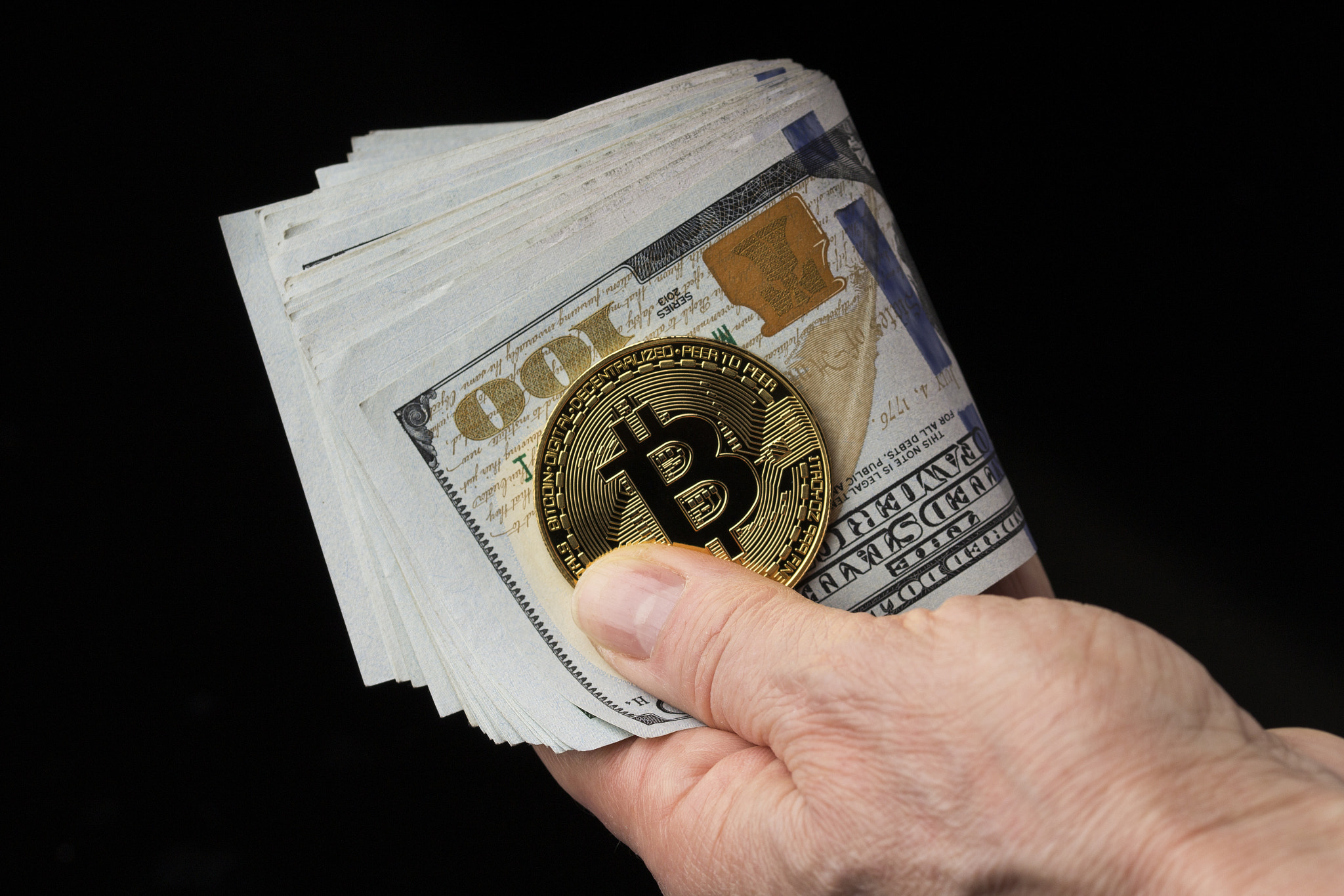 feale hand holds bitcoin and dollar bills on black background