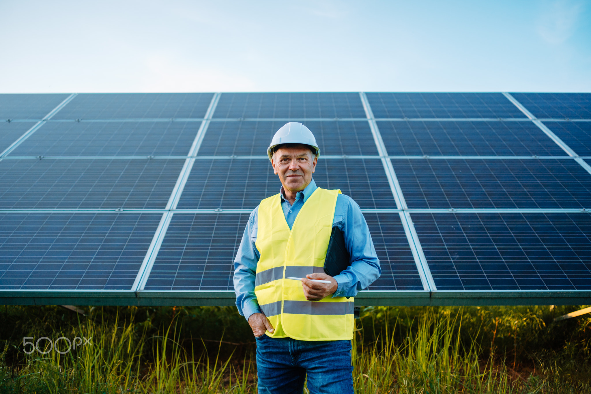 Worker or engineer stands front of solar panels looking at camera.