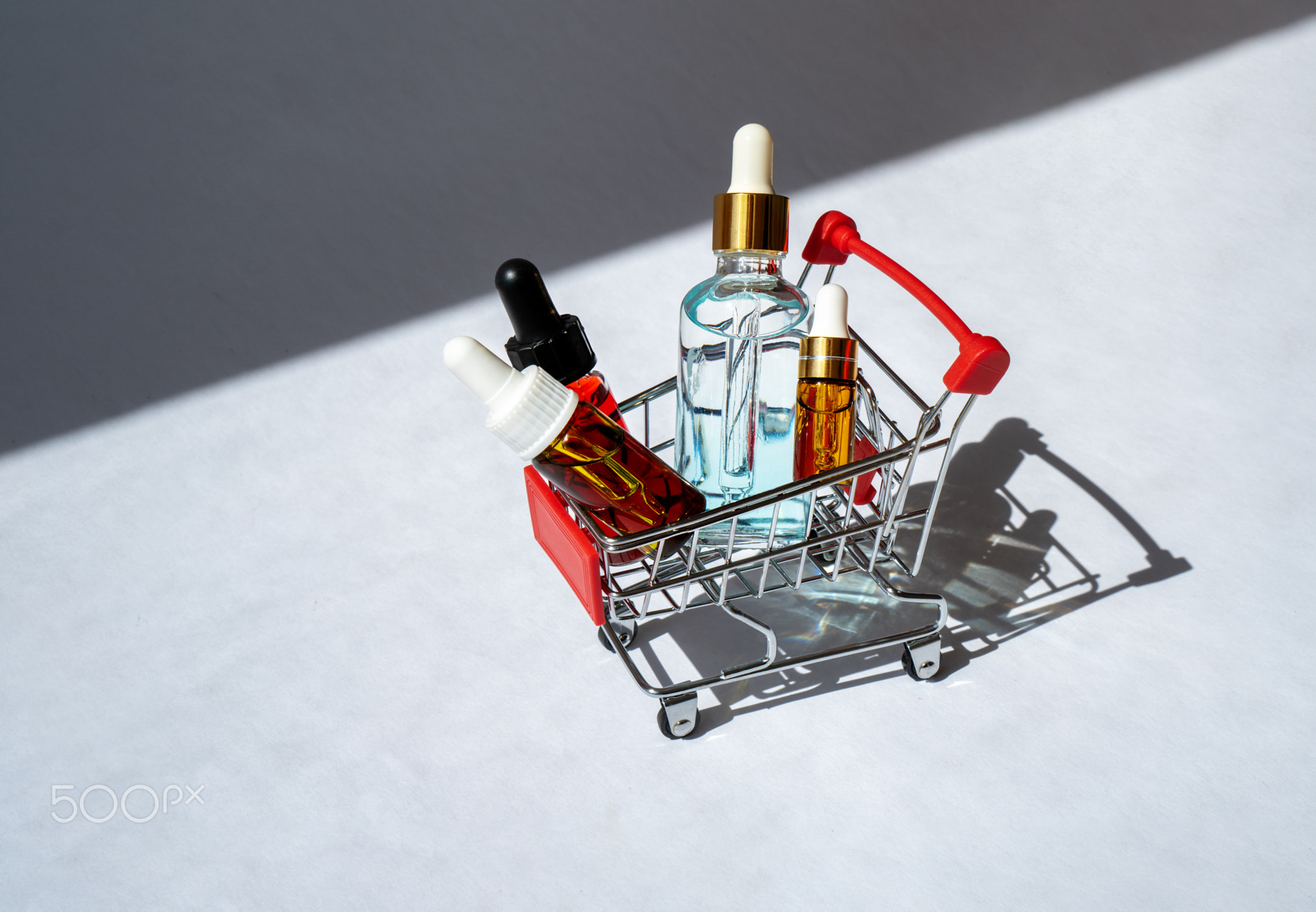Small shopping cart with cosmetic bottles. Essential oil, serum and