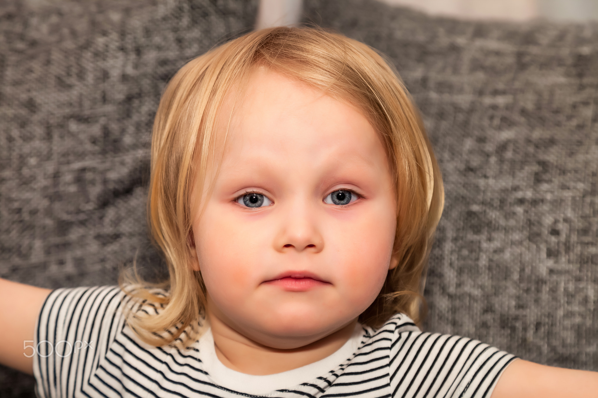 Portrait cute sad little blond baby girl three year old sitting on sofa