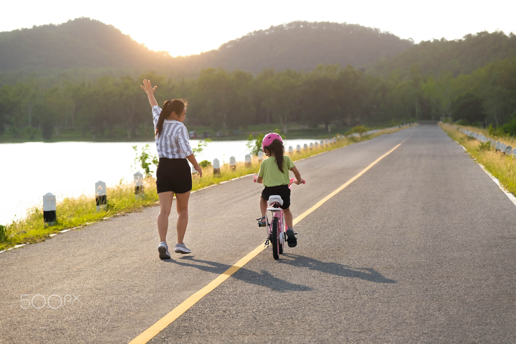 Asian mother teaching daughter to ride a bicycle in the park. A cute happy 
