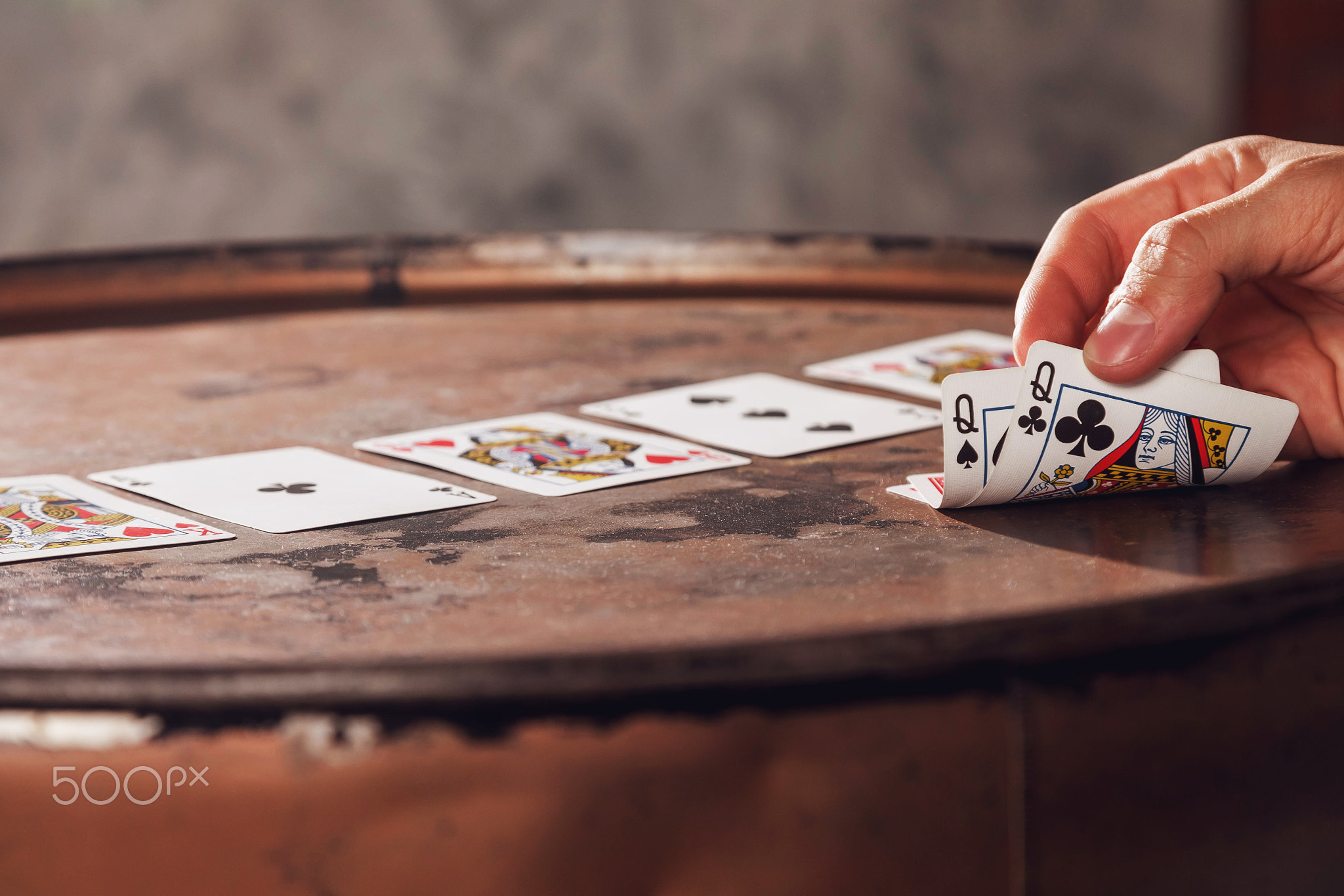 Close-up of mans hand showing his cards with two ladies card while playing poker on barrel