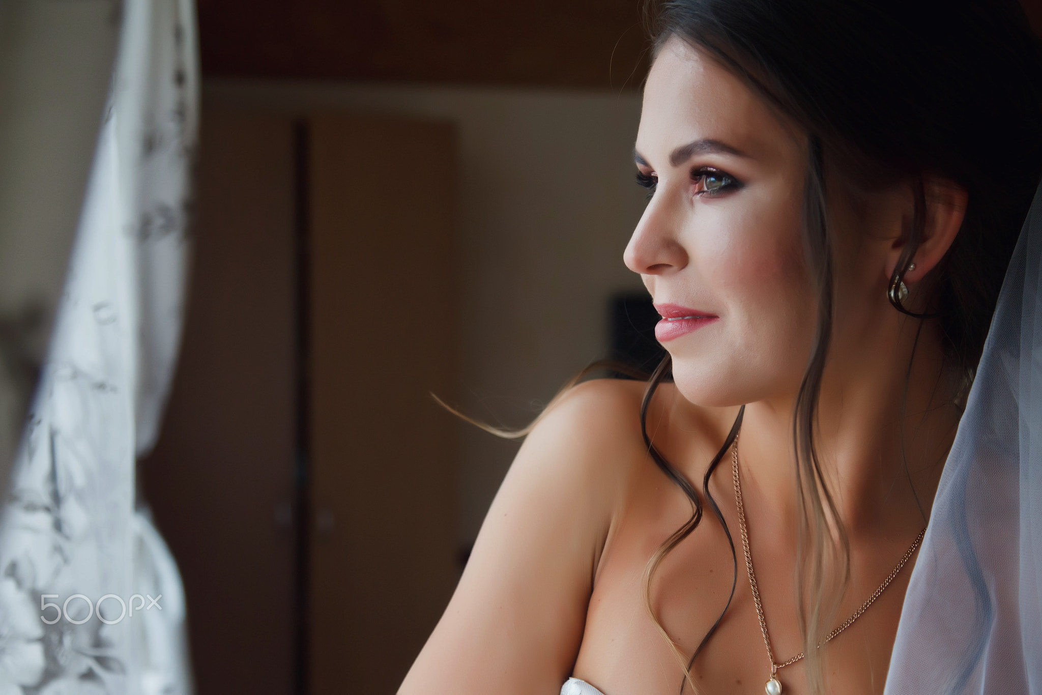 Cute young woman bride in home white dress at window in country house