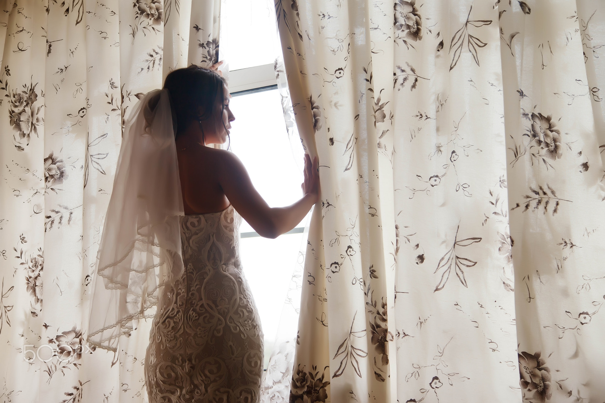 Cute young woman bride in home white dress at window in country house