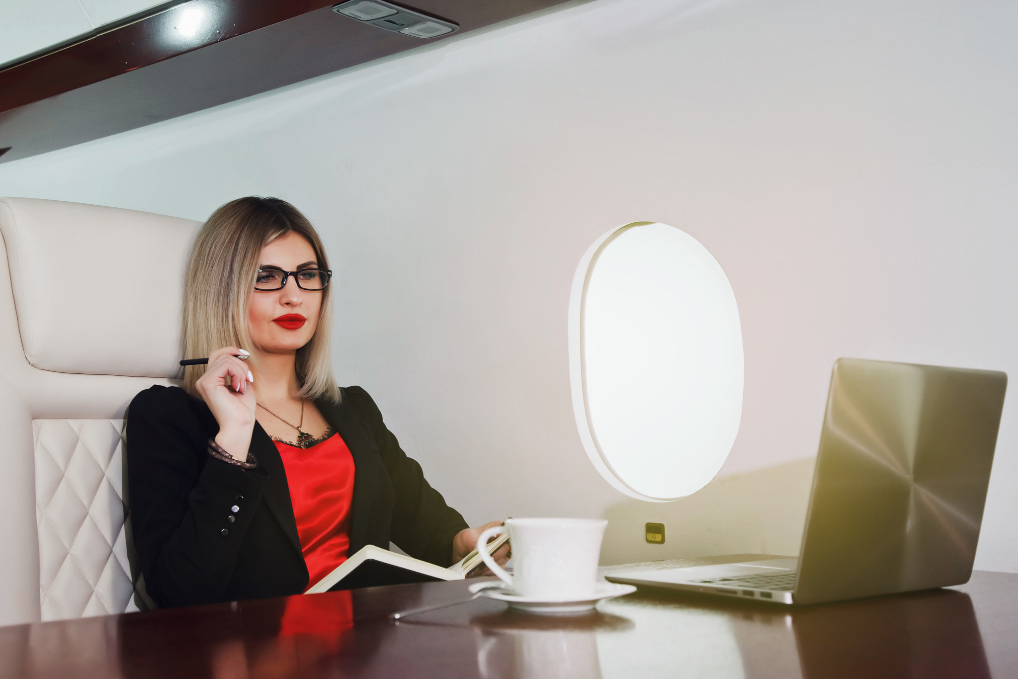 Cute young businesswoman working on laptop in luxury private jet