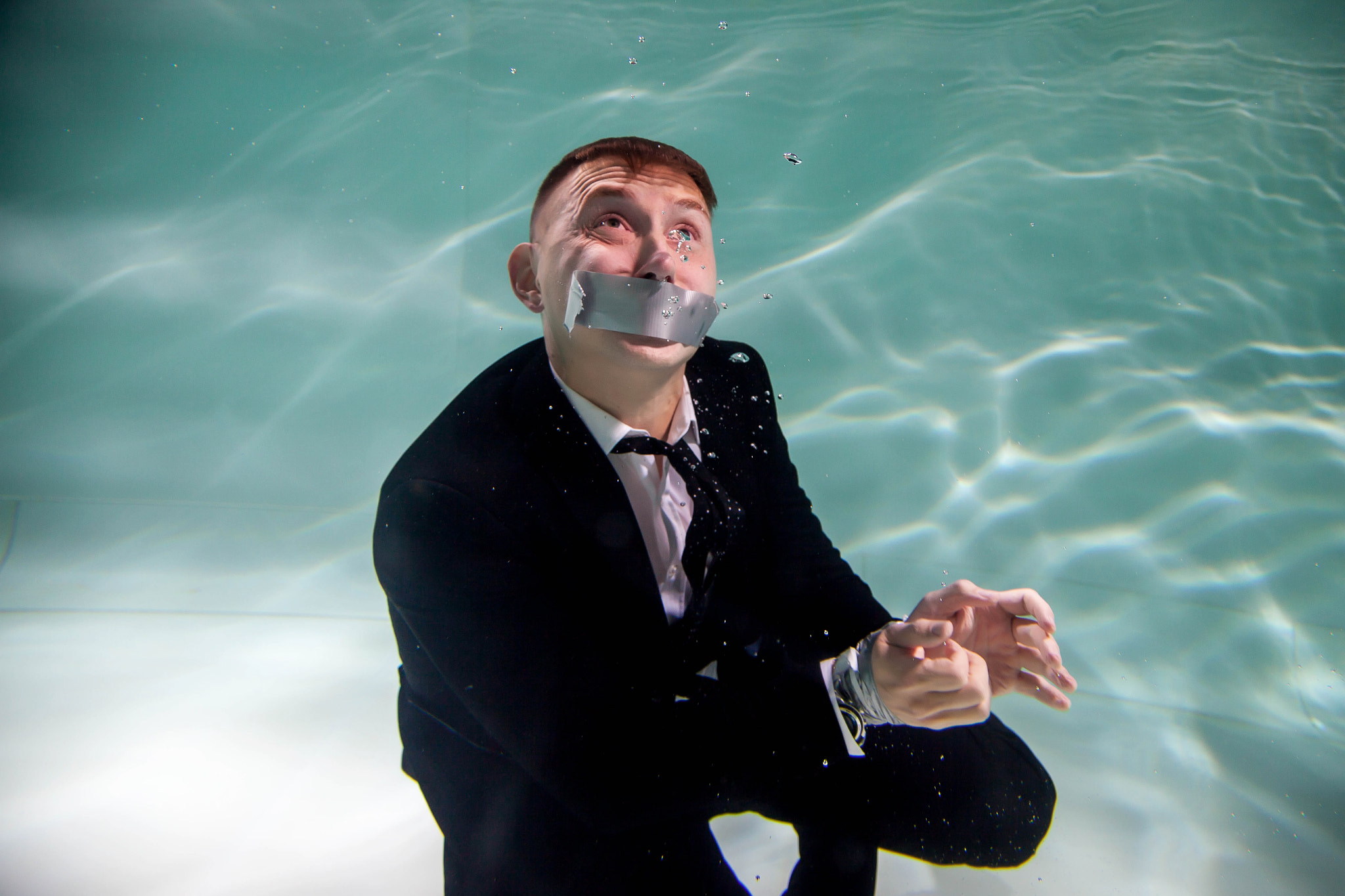 Cute successful young businessman with his mouth taped и and hands tied underwater