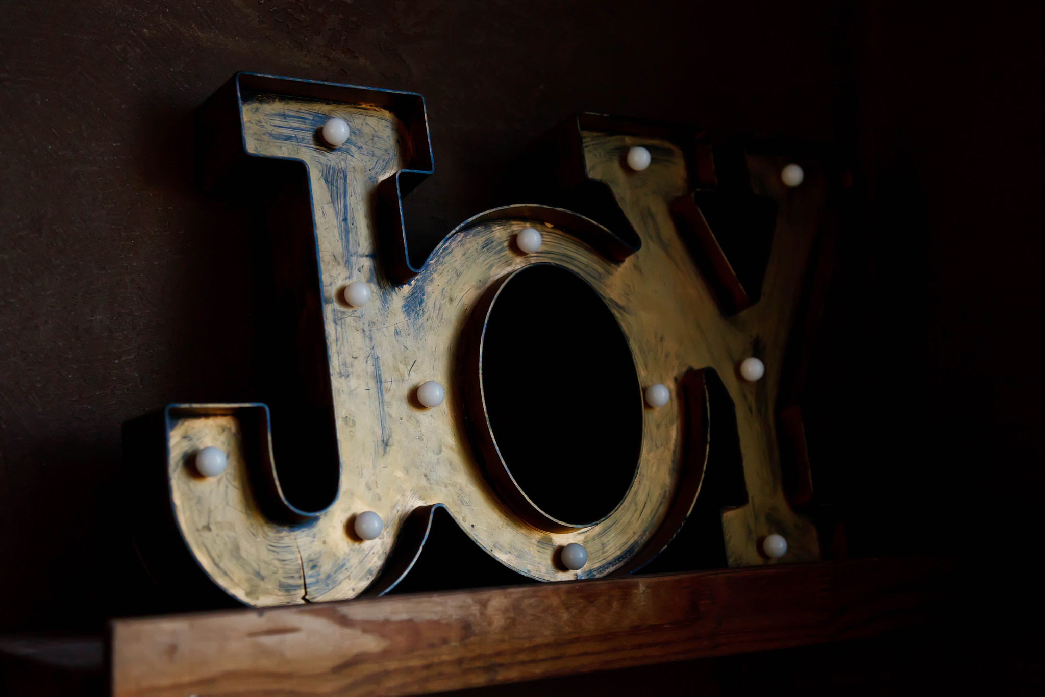 Tin letters forming word JOY on dark brown wall background