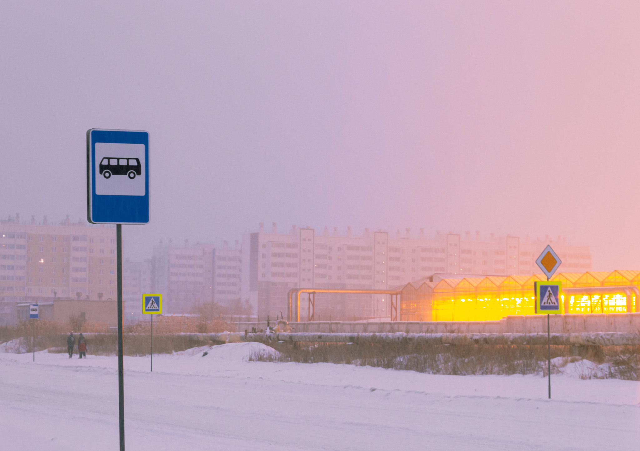 Bus stop sign against the background of the light of greenhouses, people and residential buildings